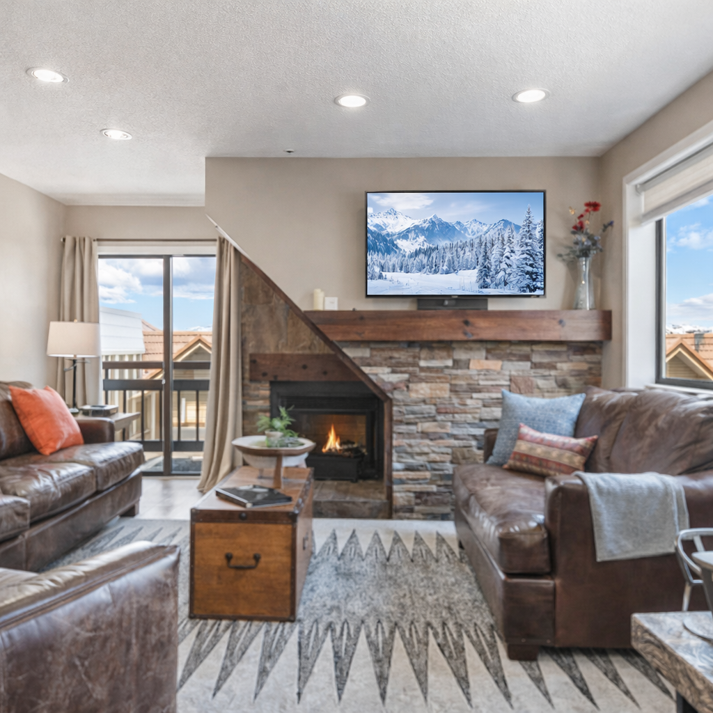 Cozy mountain living room with stone fireplace, leather seating, and flat-screen TV. Relax after skiing with scenic views, warm décor, and open layout.