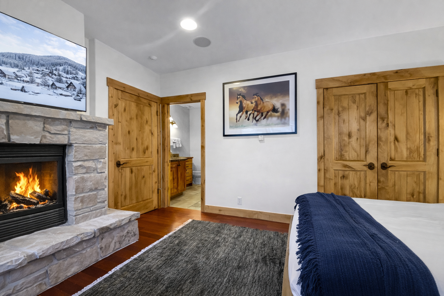 Retreat to this cozy bedroom featuring a inviting fireplace for warmth and ambiance. Relax in comfort with a large TV and natural wood doors adding a rustic touch.