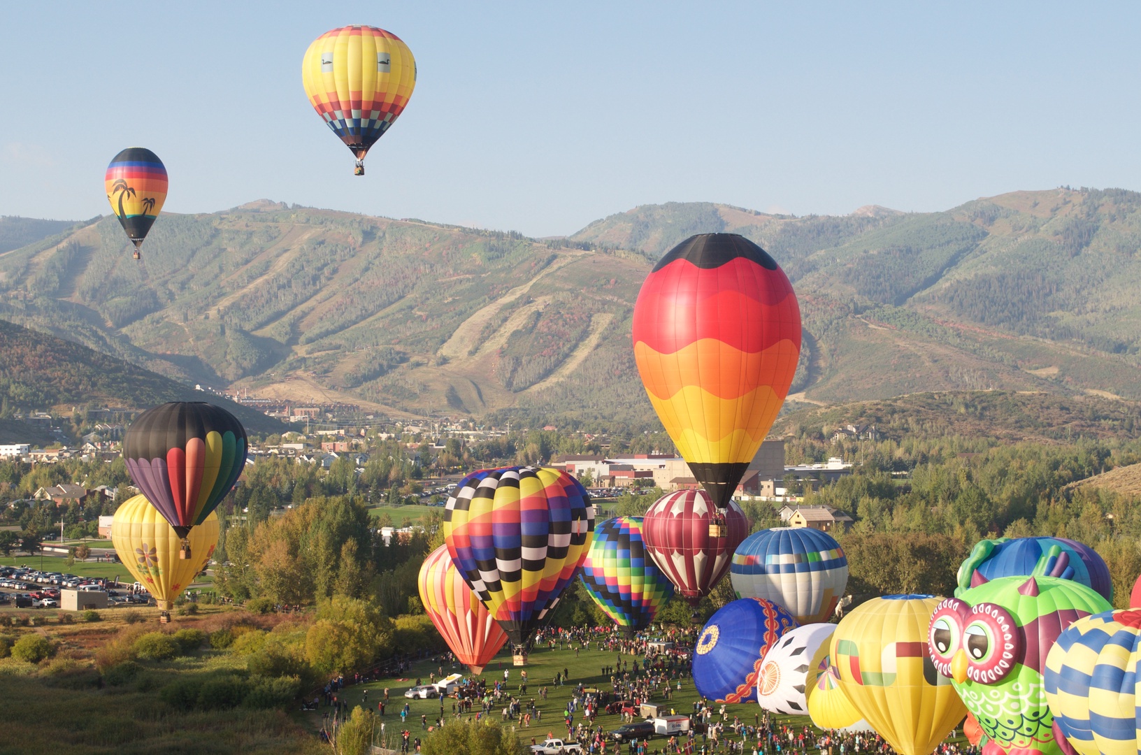 Colorful hot air balloons fill the sky above a mountain valley during the annual balloon festival in the surrounding area.