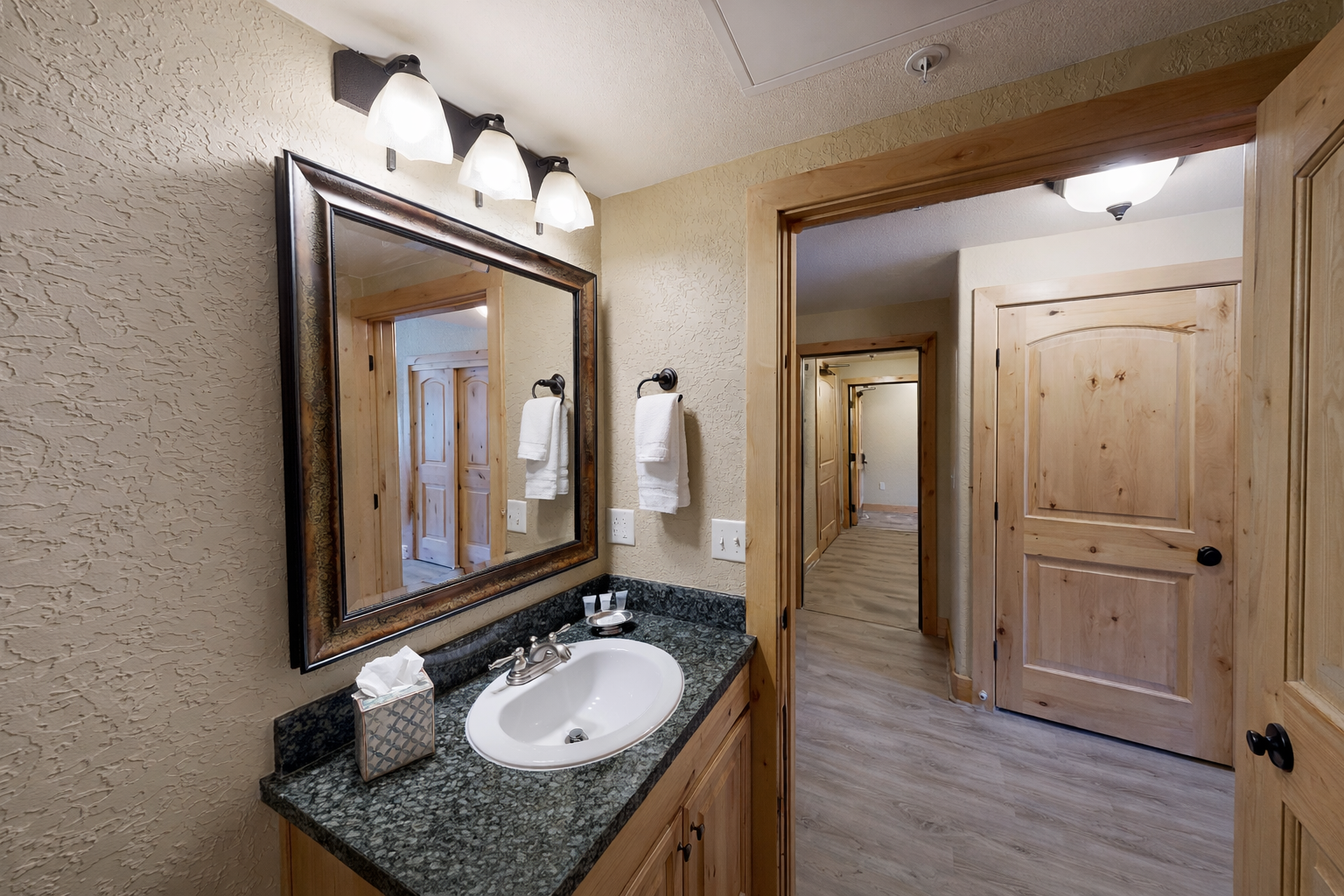This refined bathroom features a sleek granite vanity, a large framed mirror, and warm wood accents. The bright, open hallway leads you effortlessly to the rest of your retreat.