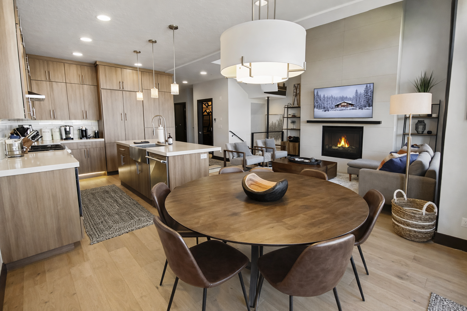 This sun-drenched open-concept space features a gourmet kitchen with a large island, a round wooden dining table for eight, and a cozy living area with a gas fireplace.