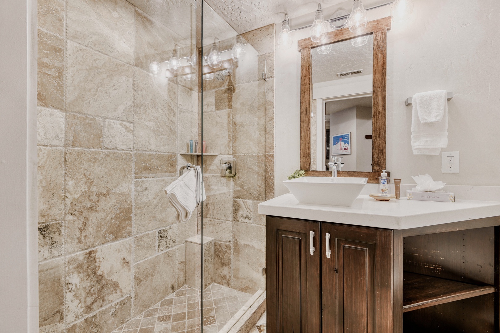 Refresh in your beautifully appointed bathroom with warm travertine tiles, glass shower, and elegant wood vanity.