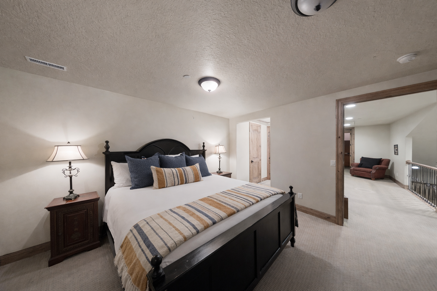 This spacious guest room features a grand four-poster bed, premium linens, and warm bedside lighting. Shuttered windows and plush carpeting create a quiet, comfortable retreat for a restful night.
