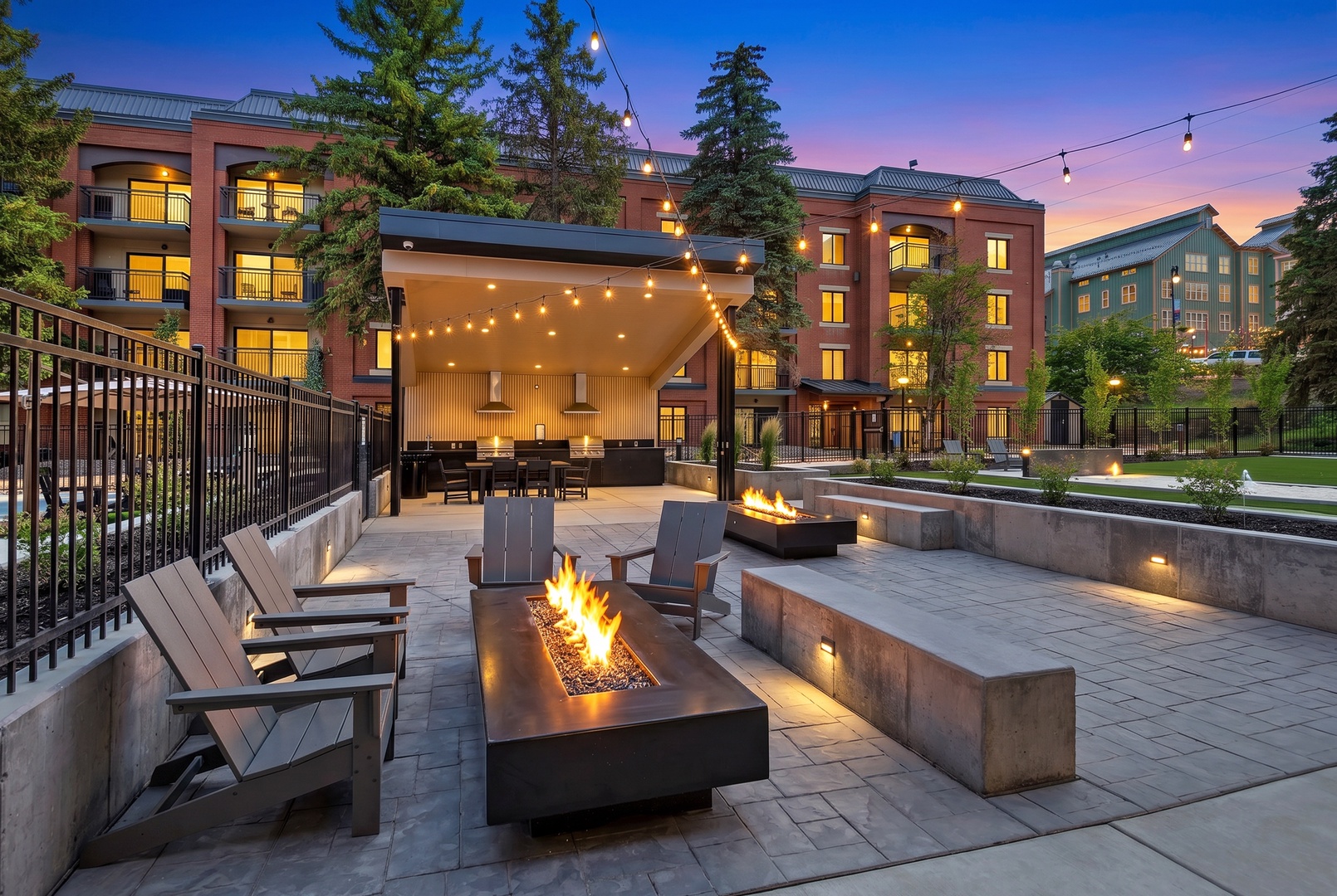 Modern property featuring multi-level accommodations set among mature evergreens, with an inviting outdoor courtyard area as dusk settles in.