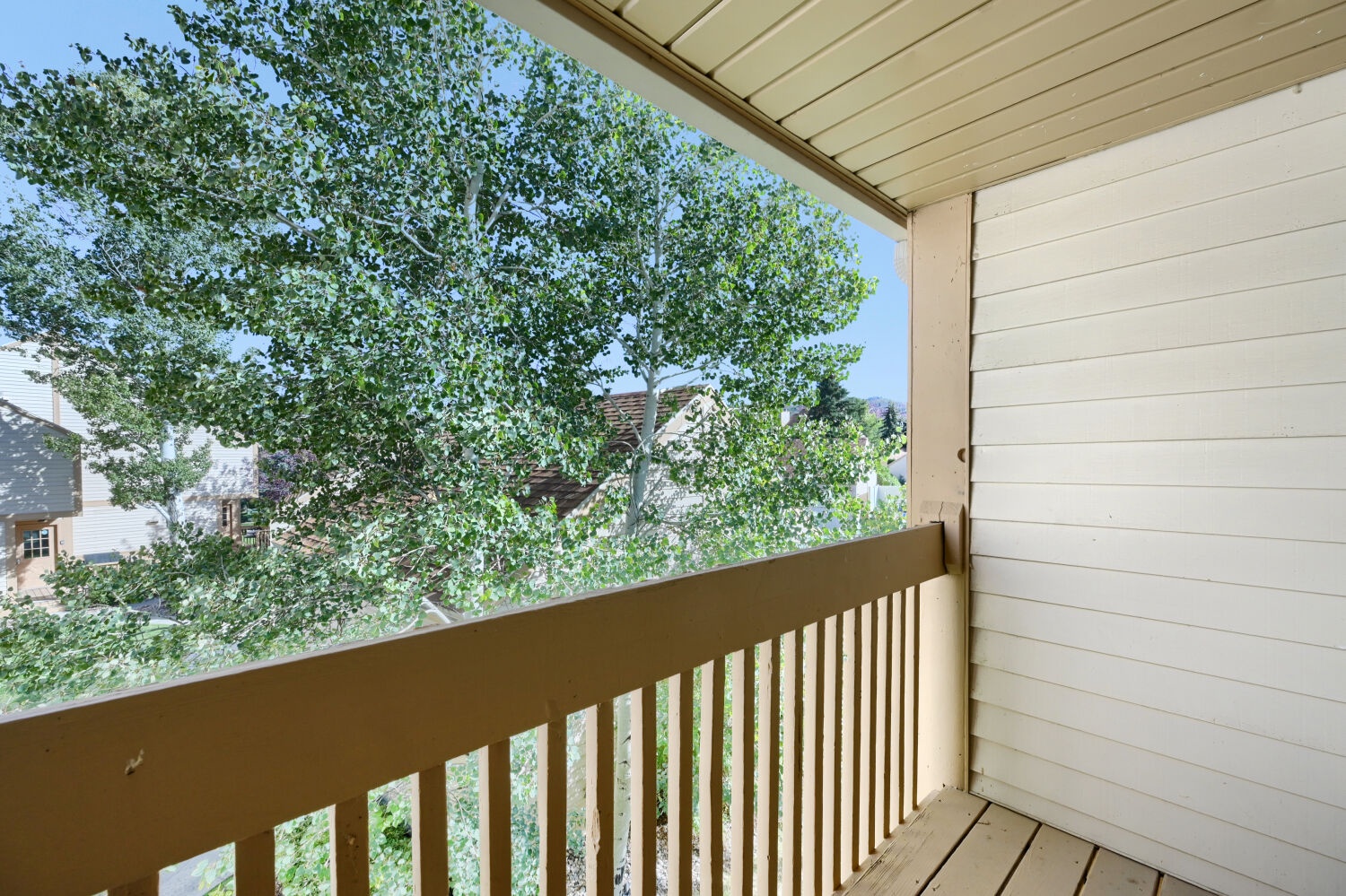 A covered balcony overlooks a peaceful neighborhood framed by leafy trees, offering a quiet spot to enjoy the surrounding residential area.