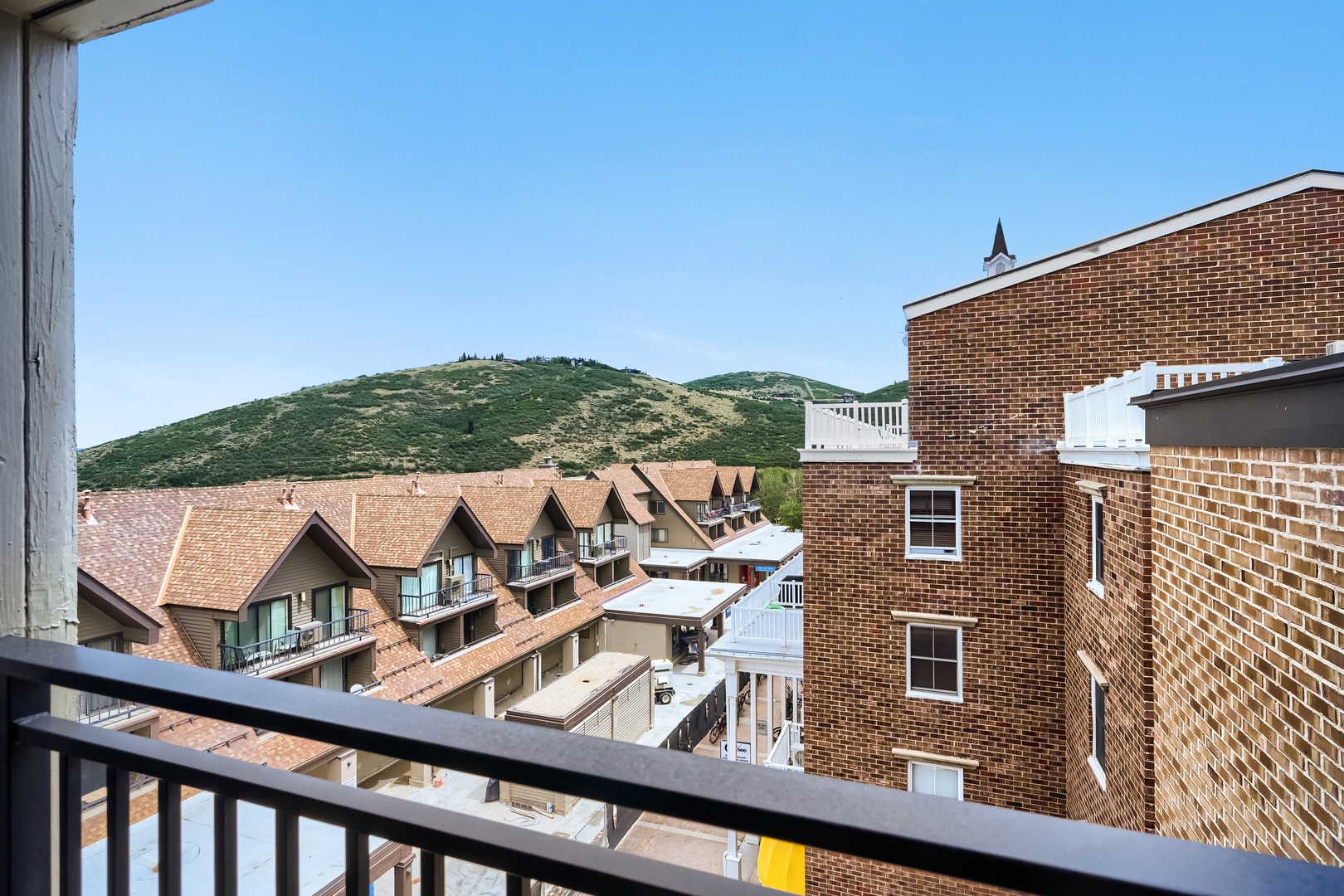 A scenic mountain backdrop frames the property, showcasing nearby rooftops and the surrounding alpine neighborhood under clear blue skies.
