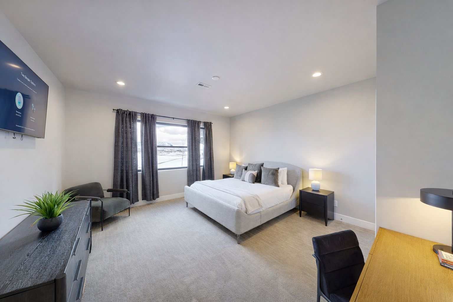 Relax in your modern bedroom with plush bedding, sleek furnishings, and a wall-mounted TV for your entertainment comfort.