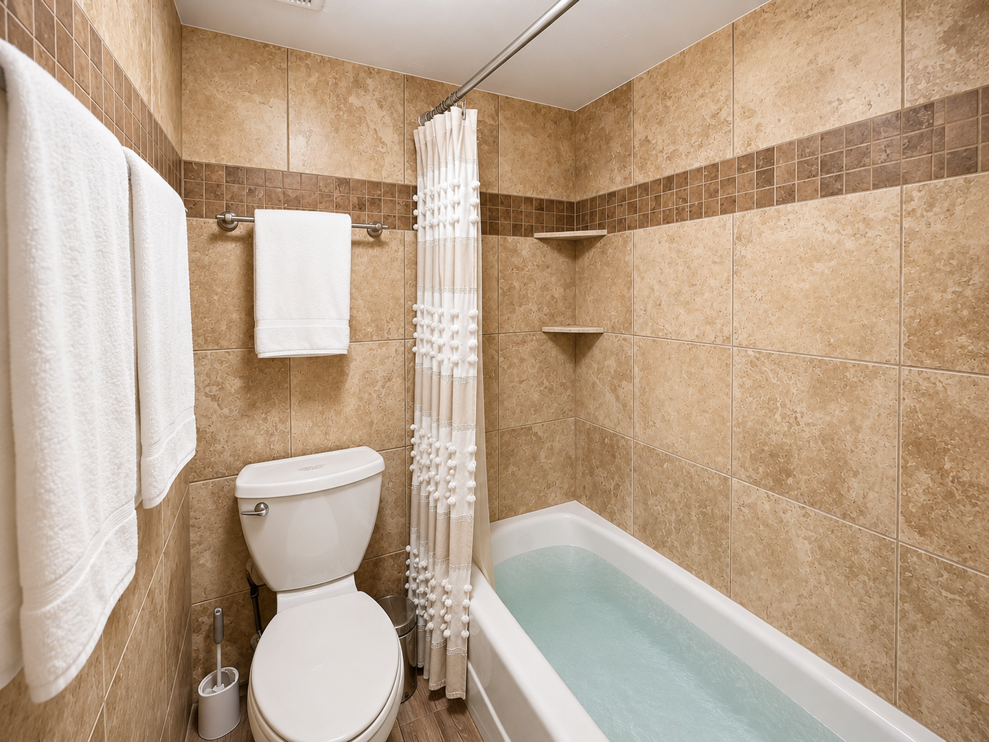 Your private bathroom features a tiled tub-shower combo with convenient built-in shelves, fresh towels, and warm neutral tones for a relaxing retreat.