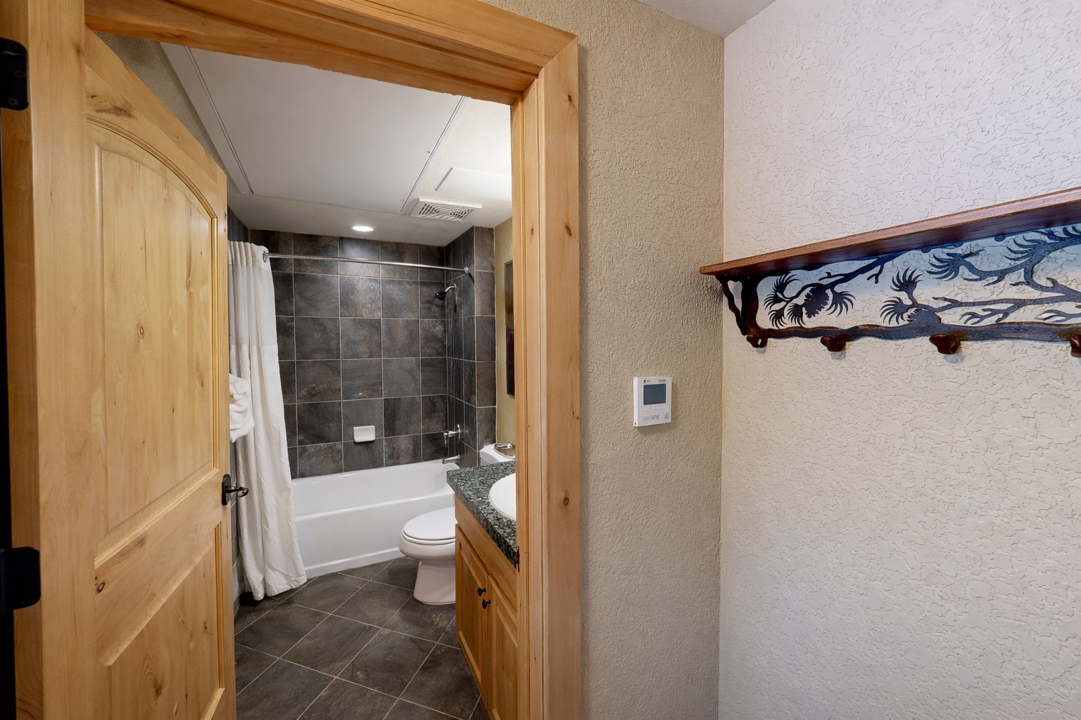 This well-appointed bathroom features a classic bathtub with dark slate tile, a natural wood vanity, and a large mirror. Modern fixtures and bright lighting ensure a comfortable, refreshing start.