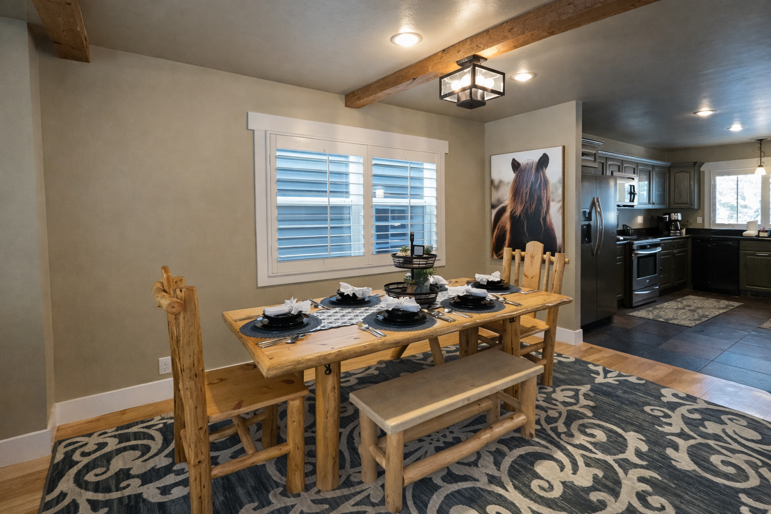 Gather around this rustic wooden dining table, featuring a mix of high-back chairs and bench seating. The space is beautifully accented with mountain-inspired decor, a patterned area rug, and soft overhead lighting.