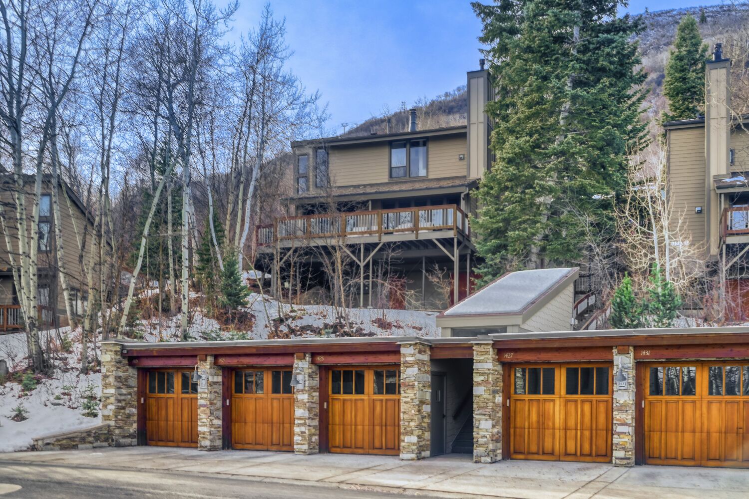 Mountain townhome with rustic stone and wood garage entrance, surrounded by evergreens and winter landscape.