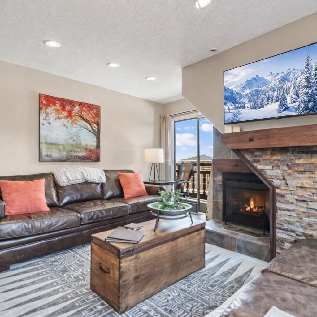 Cozy mountain living room with stone fireplace, leather seating, and smart TV. Open layout, natural light, and balcony access create the perfect Park City retreat after skiing or hiking.