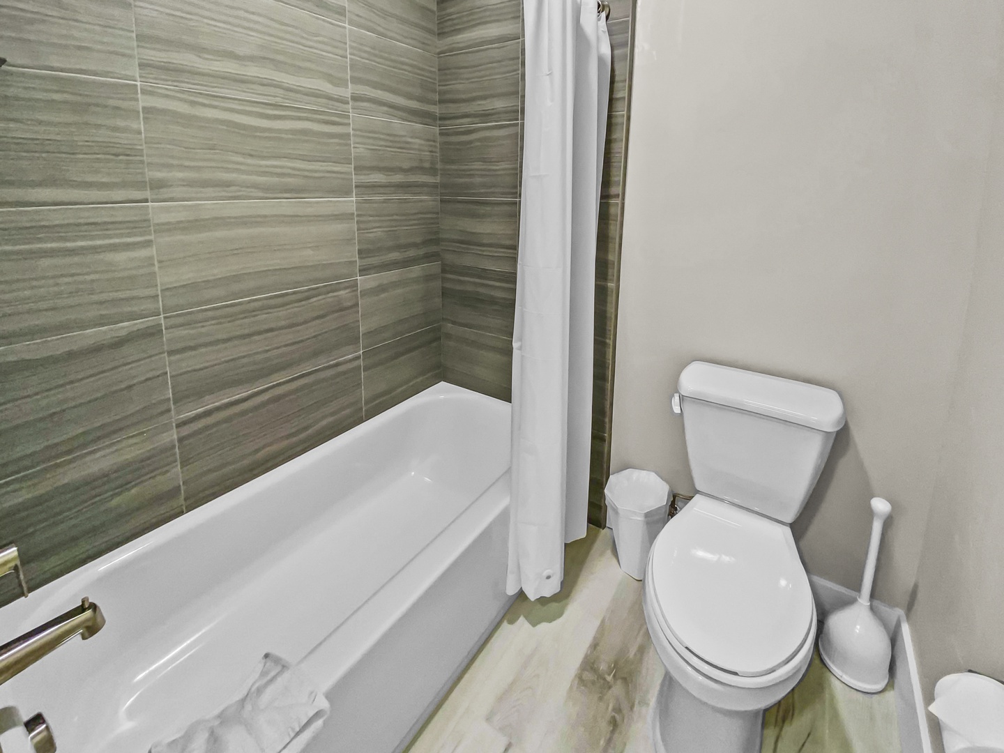 Your private bathroom combines contemporary style with functionality, featuring soothing striped tile work, a gleaming white tub and shower, and thoughtful grab bars for your safety and comfort.