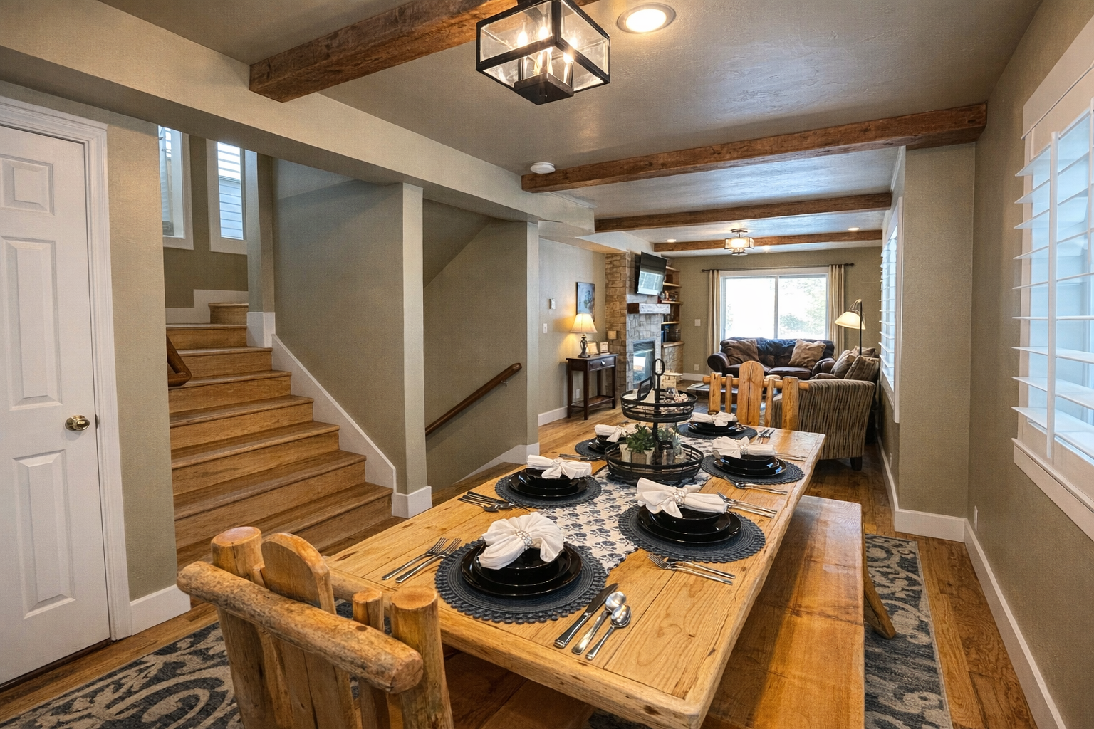 Gather around this rustic wooden dining table, featuring a mix of high-back chairs and bench seating. The space is beautifully accented with mountain-inspired decor, a patterned area rug, and soft overhead lighting.