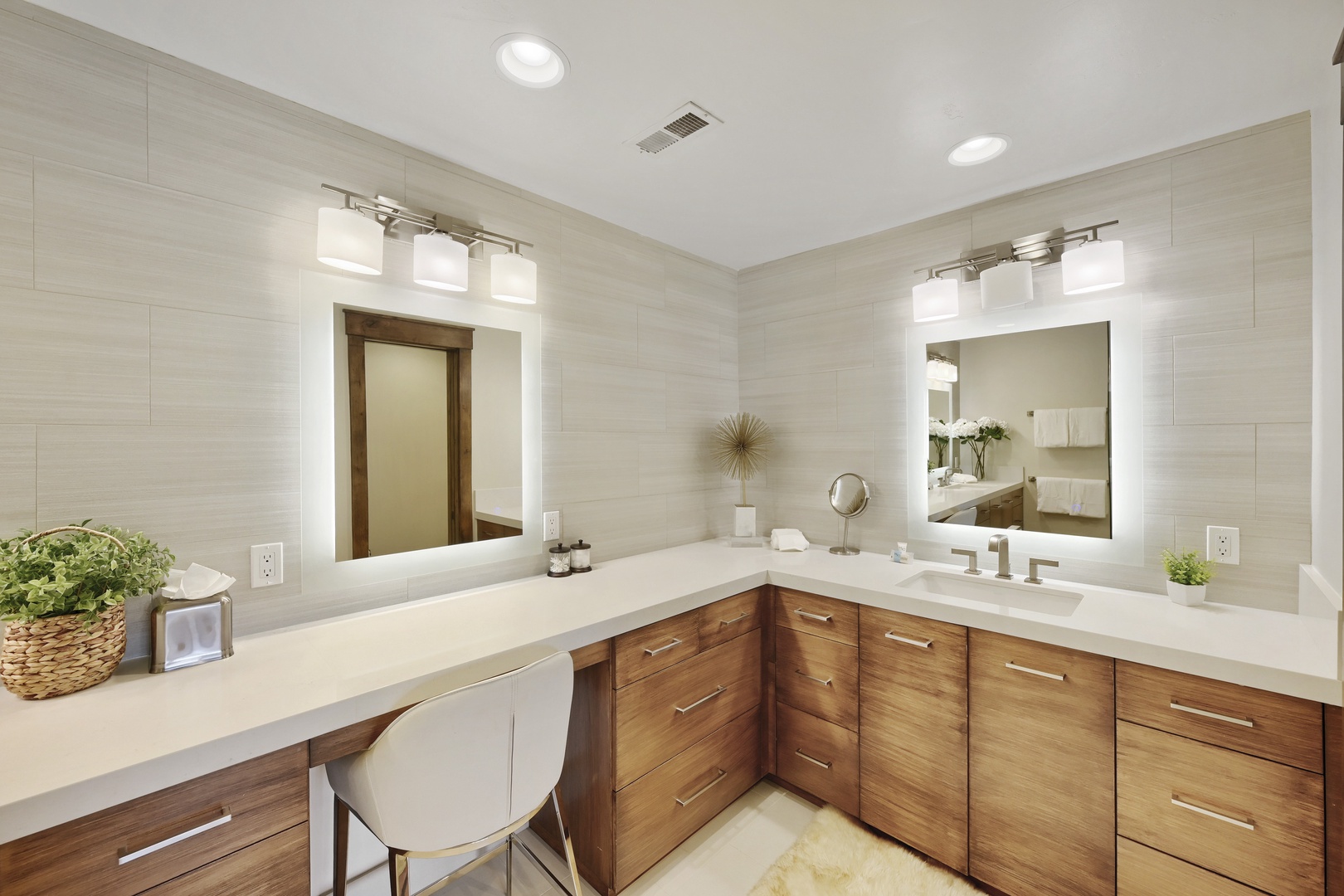 Step into your spacious private bathroom, where warm wood cabinetry meets crisp white countertops and designer lighting creates the perfect setting for your morning routine.