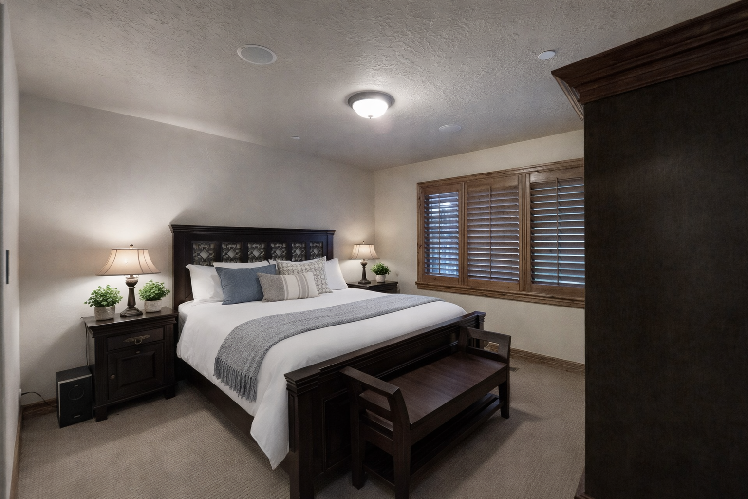 Unwind in this serene primary suite featuring a plush king bed, rich dark wood furnishings, and warm lighting. Large shuttered windows and soft neutral tones create a peaceful mountain sanctuary.