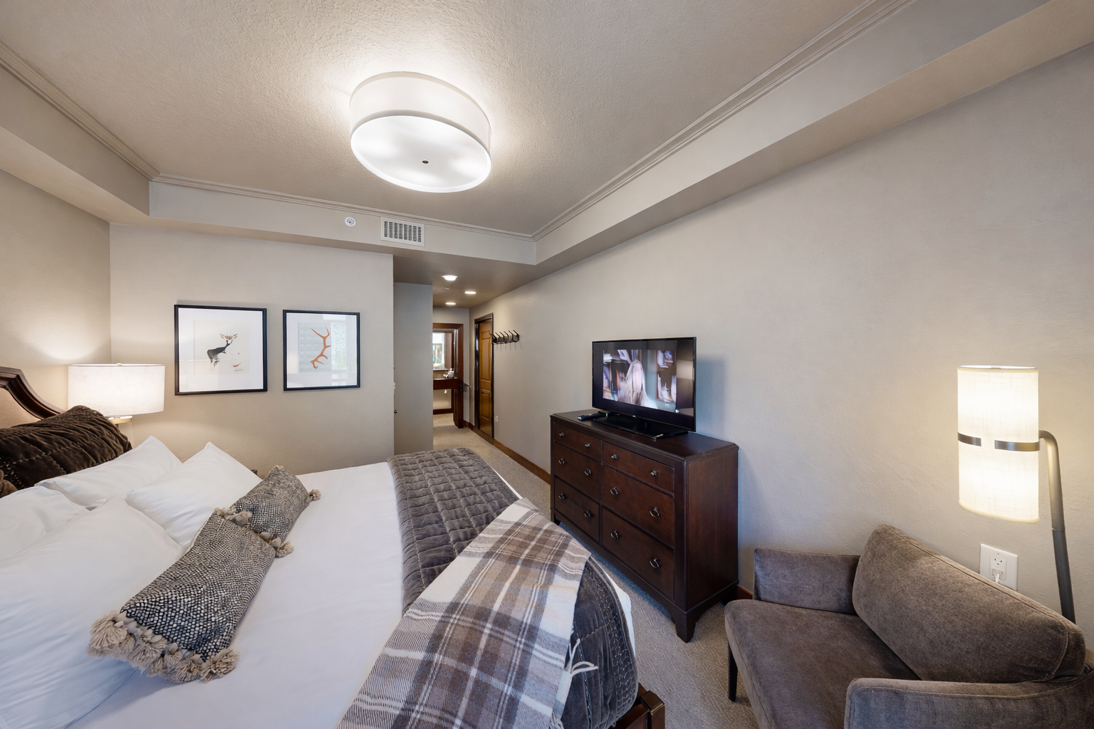 This spacious bedroom features a plush king-size bed with an elegant dark wood frame. Sliding glass doors open to a private balcony, offering stunning mountain views and plenty of natural light.