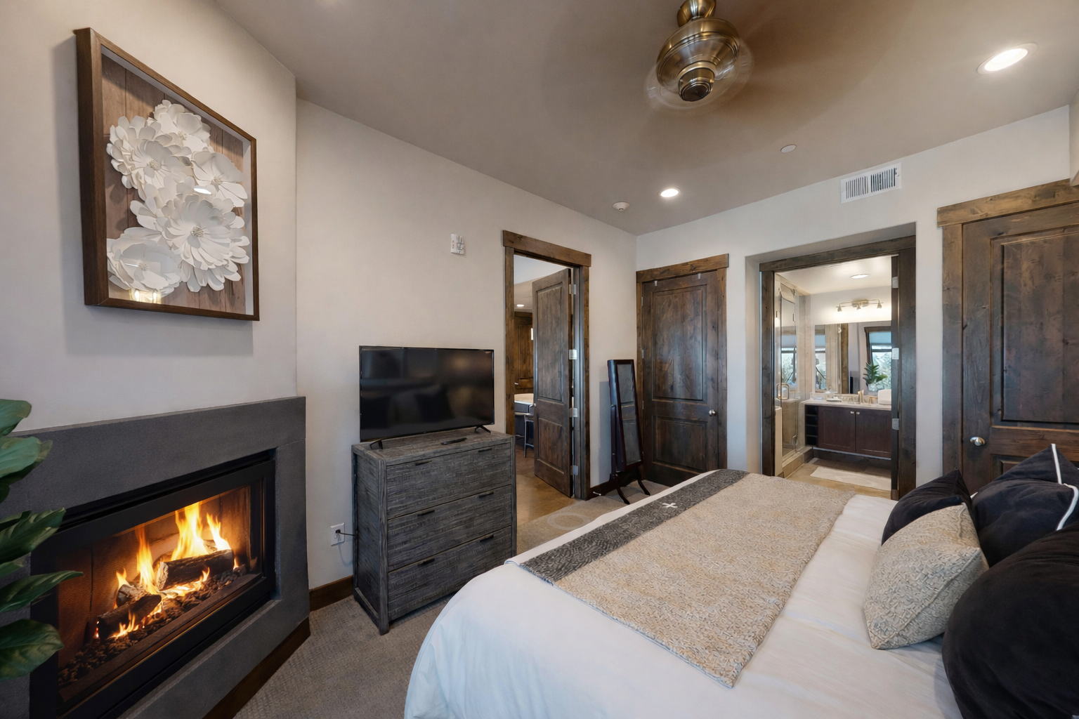 Unwind in your cozy bedroom with crackling fireplace warmth, modern amenities, and rustic wood accents creating the perfect mountain retreat atmosphere.