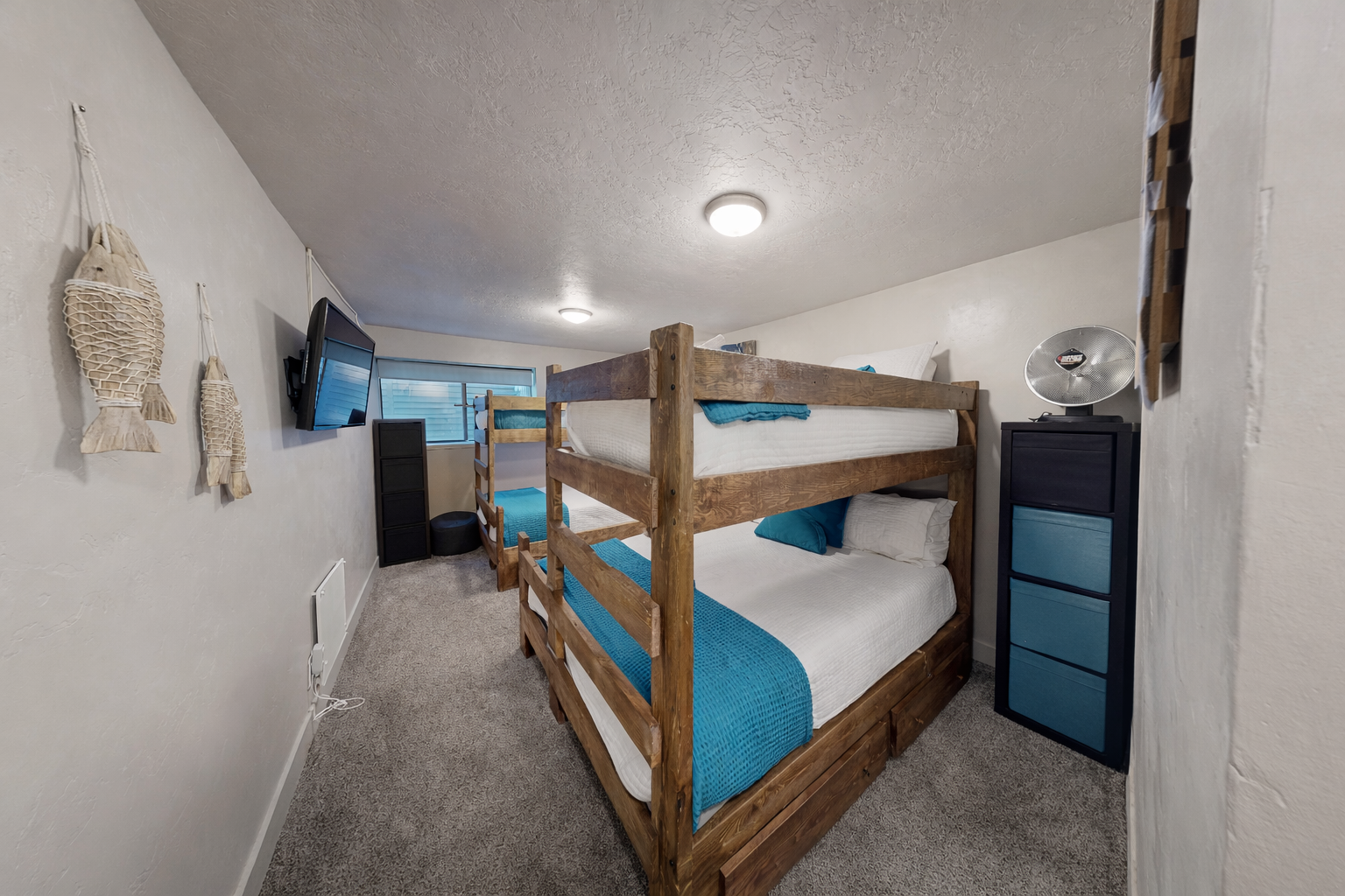 Perfect for families or groups! This custom bunk room features two twin-over-queen wooden beds, a wall-mounted TV, and bright teal accents for a fun and functional stay.