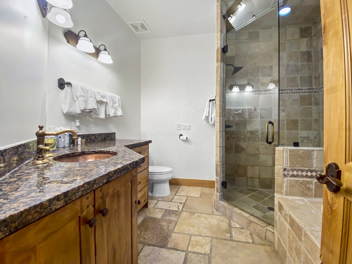 Step into this inviting bathroom featuring a rustic wood vanity with a stylish copper sink set in a granite countertop. A spacious glass-enclosed walk-in shower completes the serene, natural aesthetic.