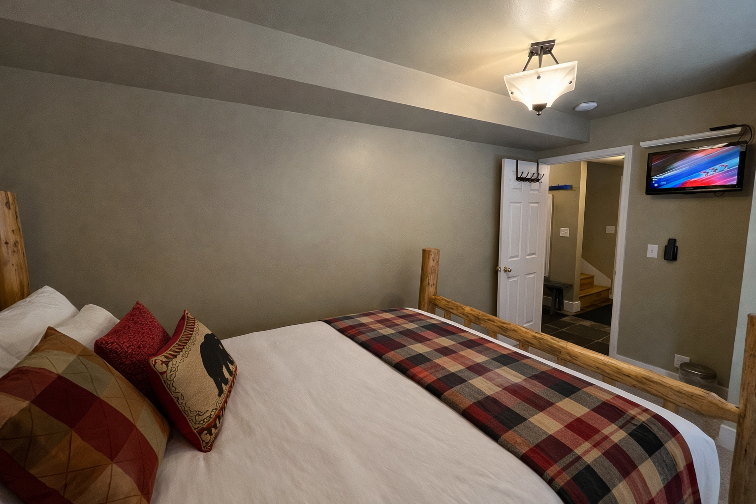 This charming secondary bedroom features a handcrafted log bed frame and cozy buffalo plaid accents. Large windows fill the space with natural light, creating a warm, inviting atmosphere for guests.