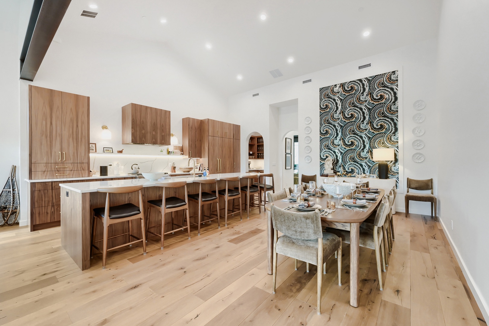 Bright, open-concept kitchen and dining area with an oversized island, soaring vaulted ceilings, rich walnut cabinetry, and warm wood floors—perfect for mornings and gatherings with loved ones.
