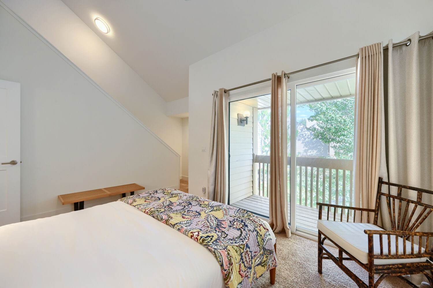 Wake up to natural light streaming through large windows that open onto your private balcony. The cozy bedroom offers a peaceful retreat with crisp linens and a touch of home-like charm, surrounded by lush greenery just outside.