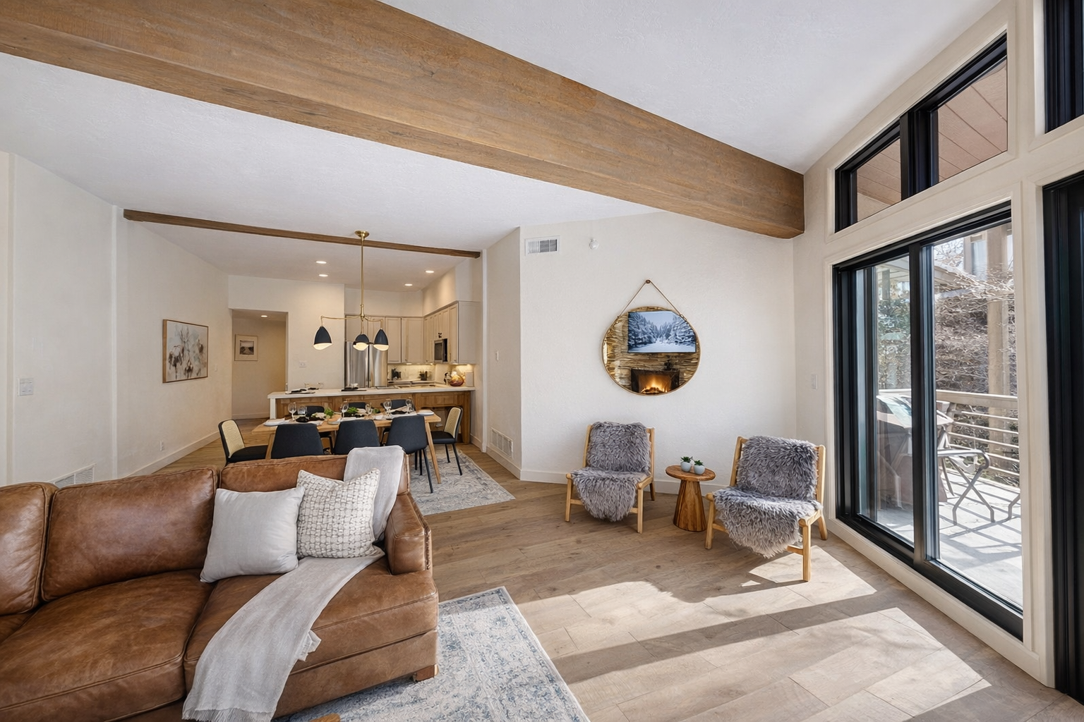 Sink into the warm leather sofa and feel the sunlight streaming through floor-to-ceiling windows as exposed beams create cozy charm above.