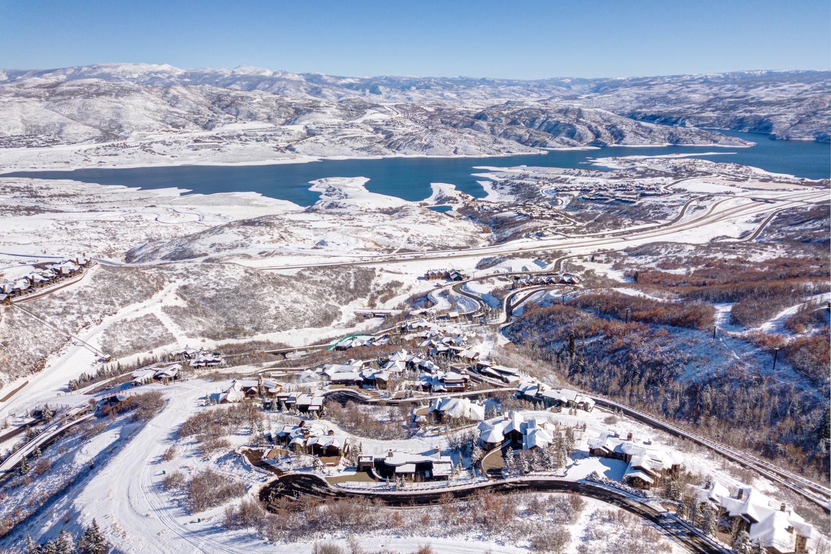 Stunning winter aerial view showcasing snow-covered mountains and pristine lake waters in the surrounding landscape.