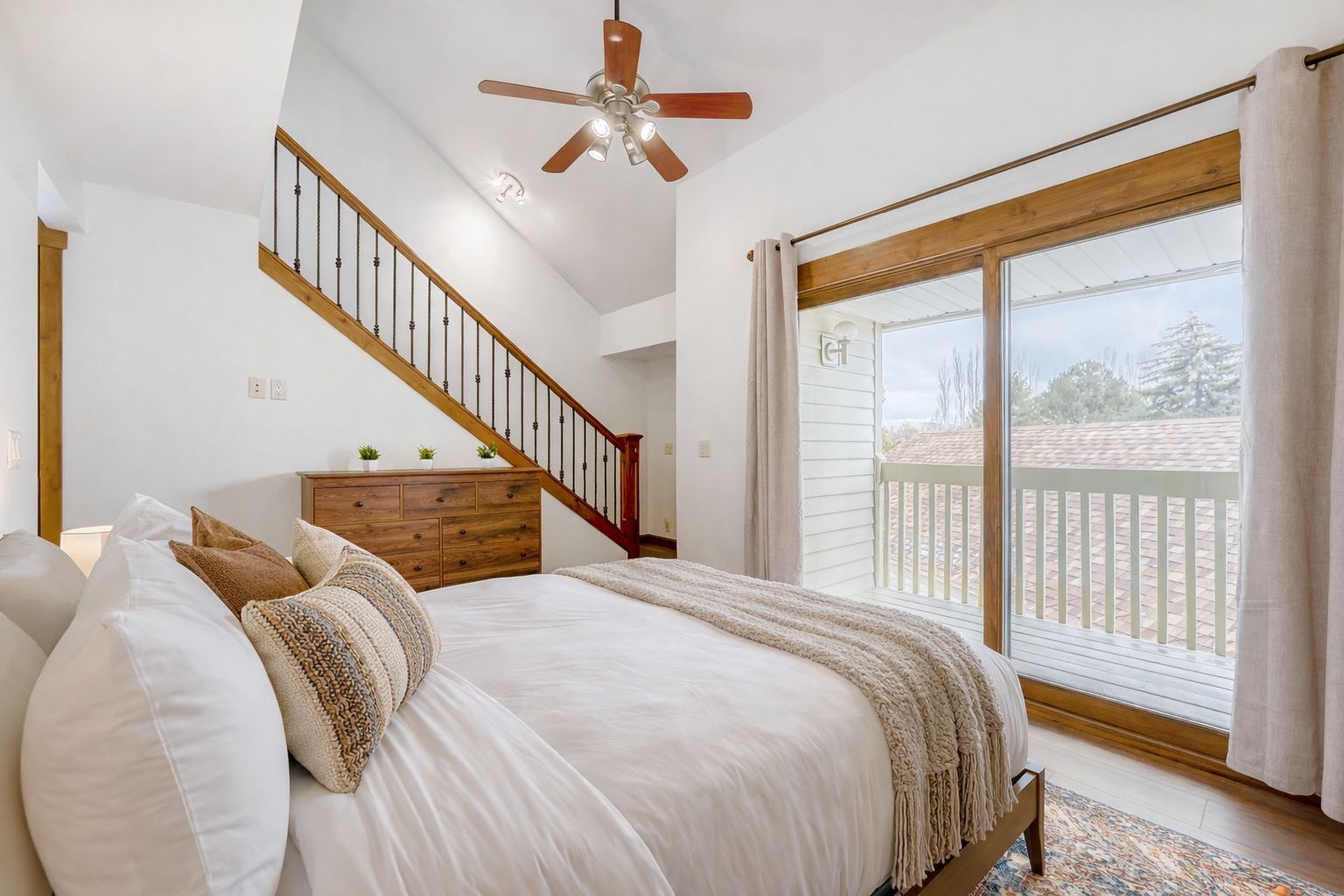 Sink into crisp white linens in your bright bedroom, where natural light streams through large windows and a ceiling fan keeps you cool.