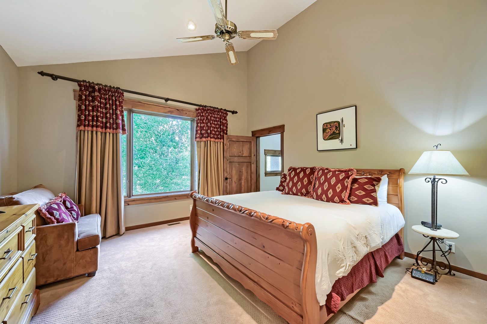 Unwind in your private bedroom featuring a beautiful wooden sleigh bed, charming décor, and a window framing peaceful greenery outside. Vaulted ceilings and warm lighting create a cozy retreat after exploring.