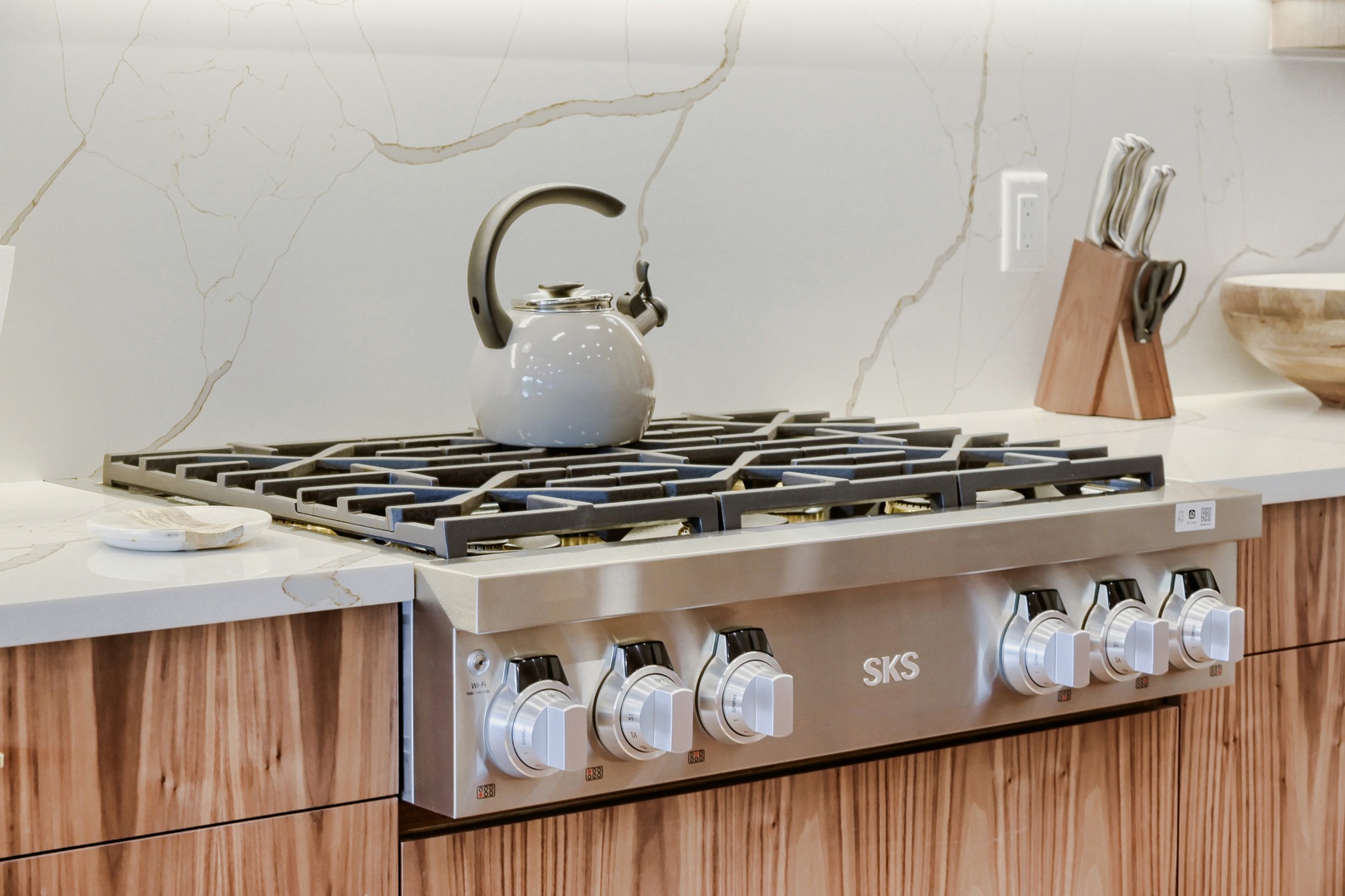 Prepare your favorite meals on this professional gas range, paired with elegant marble backsplash and modern wood cabinetry for a stylish cooking experience.