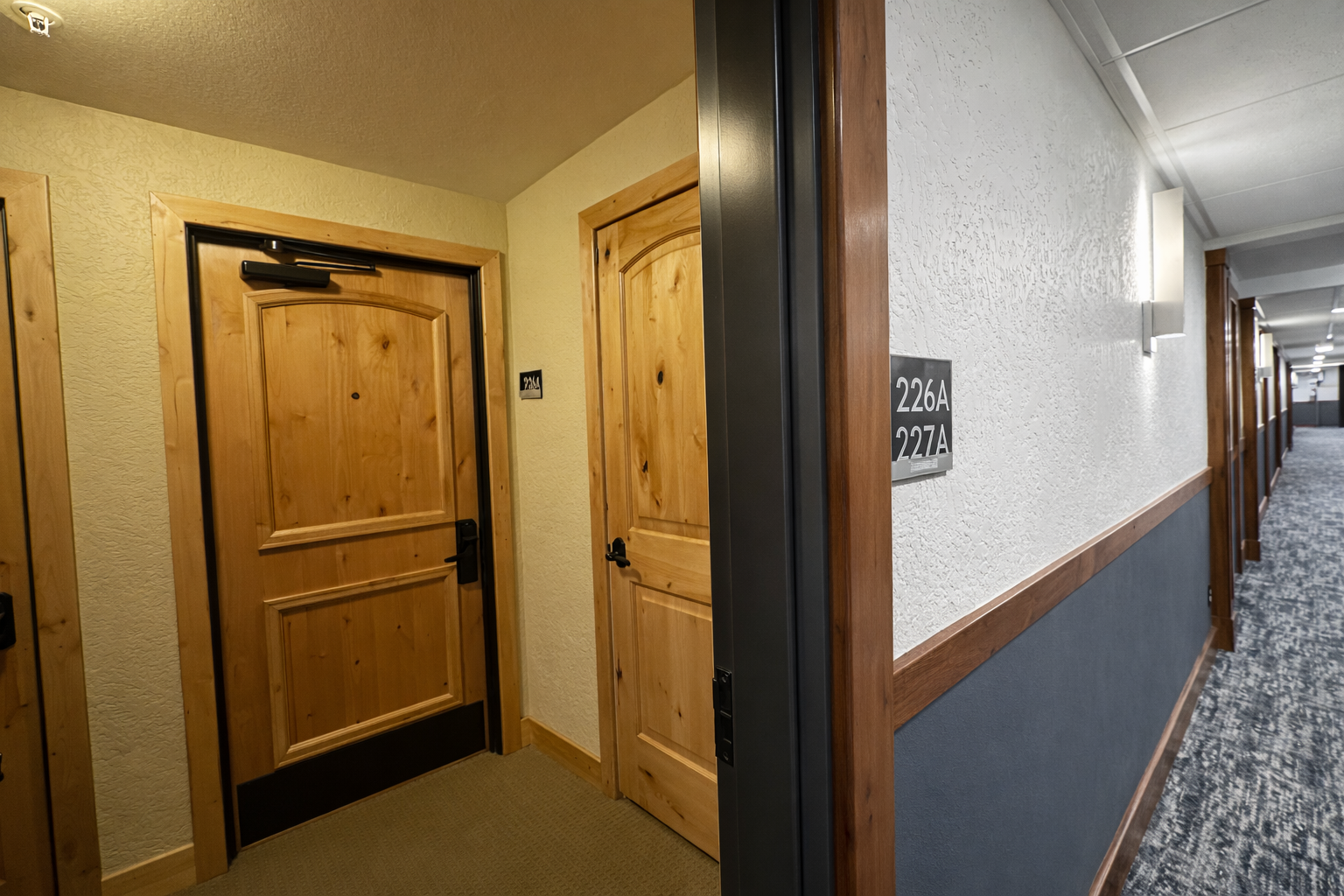 Walk through well-lit hallways with warm wood accents and carpeted floors leading to your comfortable accommodation.