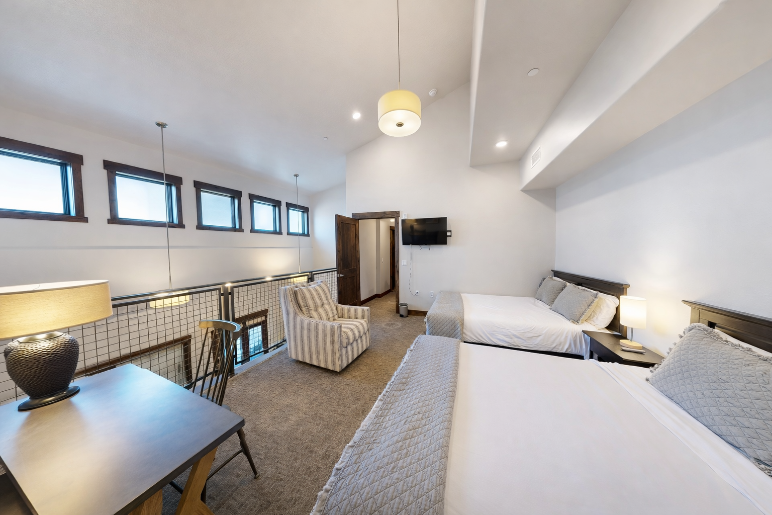 Relax in this bright and spacious bedroom featuring two plush queen beds, vaulted ceilings, and an integrated workspace. This versatile retreat offers a cozy armchair and modern art accents, perfect for families or groups.