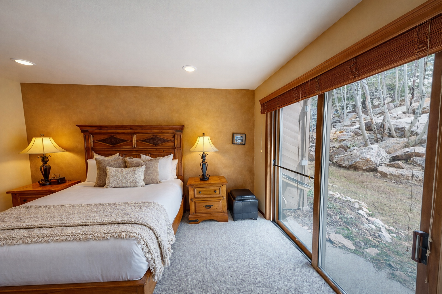 Drift off peacefully in your cozy bedroom overlooking a serene natural landscape through expansive windows.