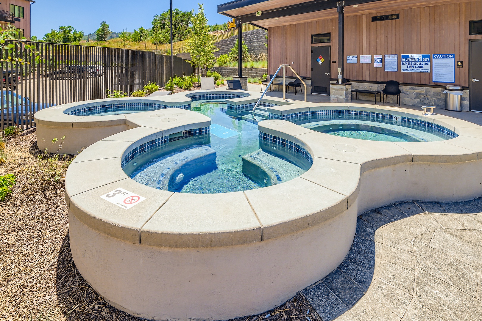 Outdoor communal hot tub and spa area with multiple soaking pools surrounded by landscaping and hillside views, offering a shared relaxation facility for guests.