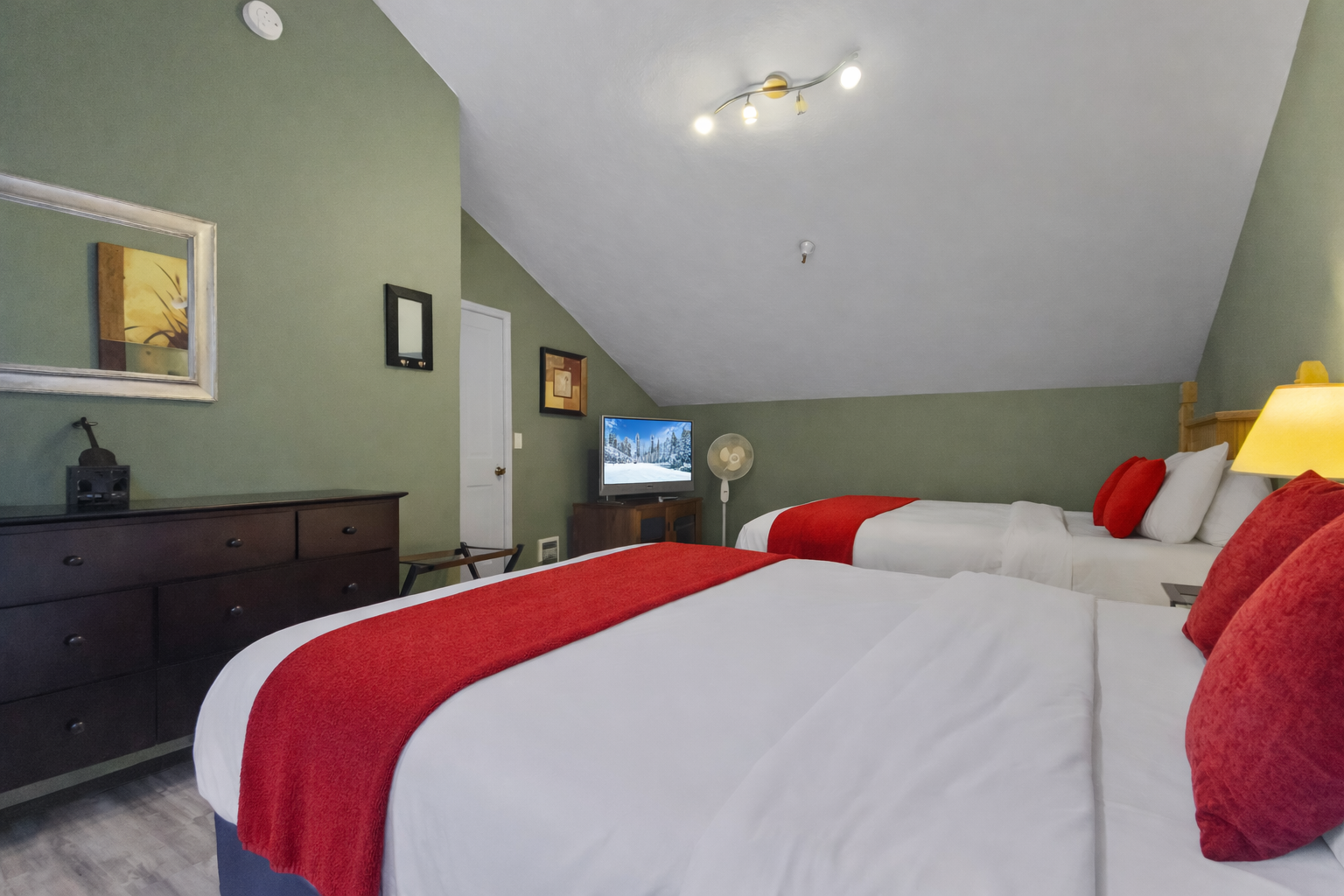 Relax in your spacious twin bedroom featuring crisp linens with vibrant red accents, modern amenities, and warm lighting for a cozy retreat.