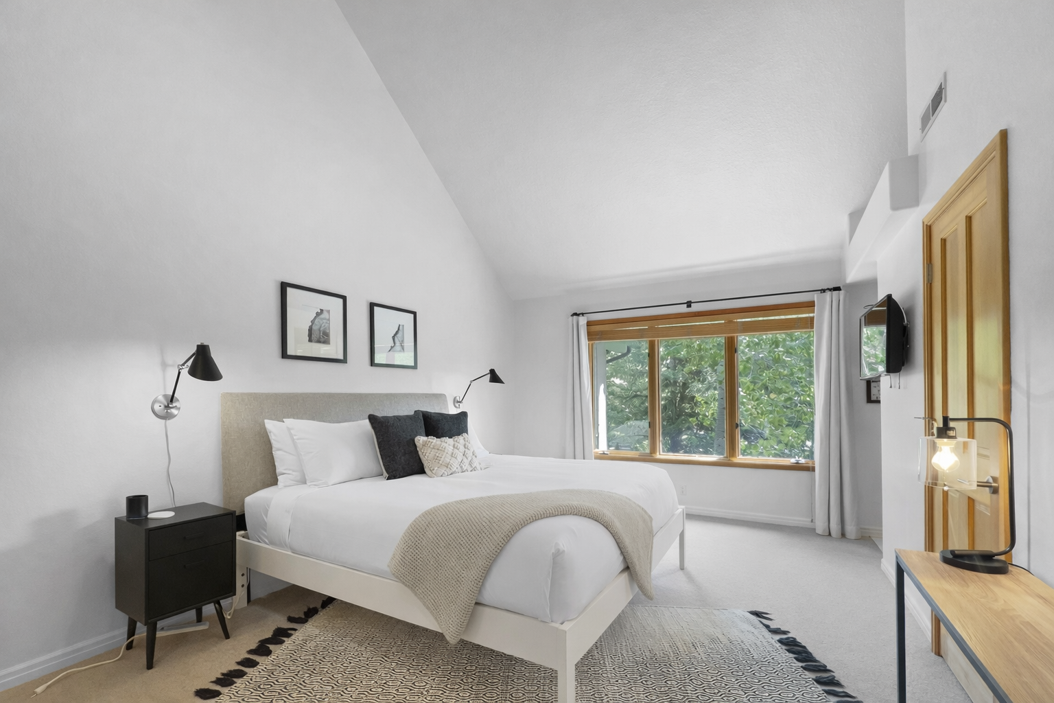 Retreat to this tranquil bedroom featuring a plush king-sized bed, a bright vaulted ceiling, and views of lush greenery for a serene escape.