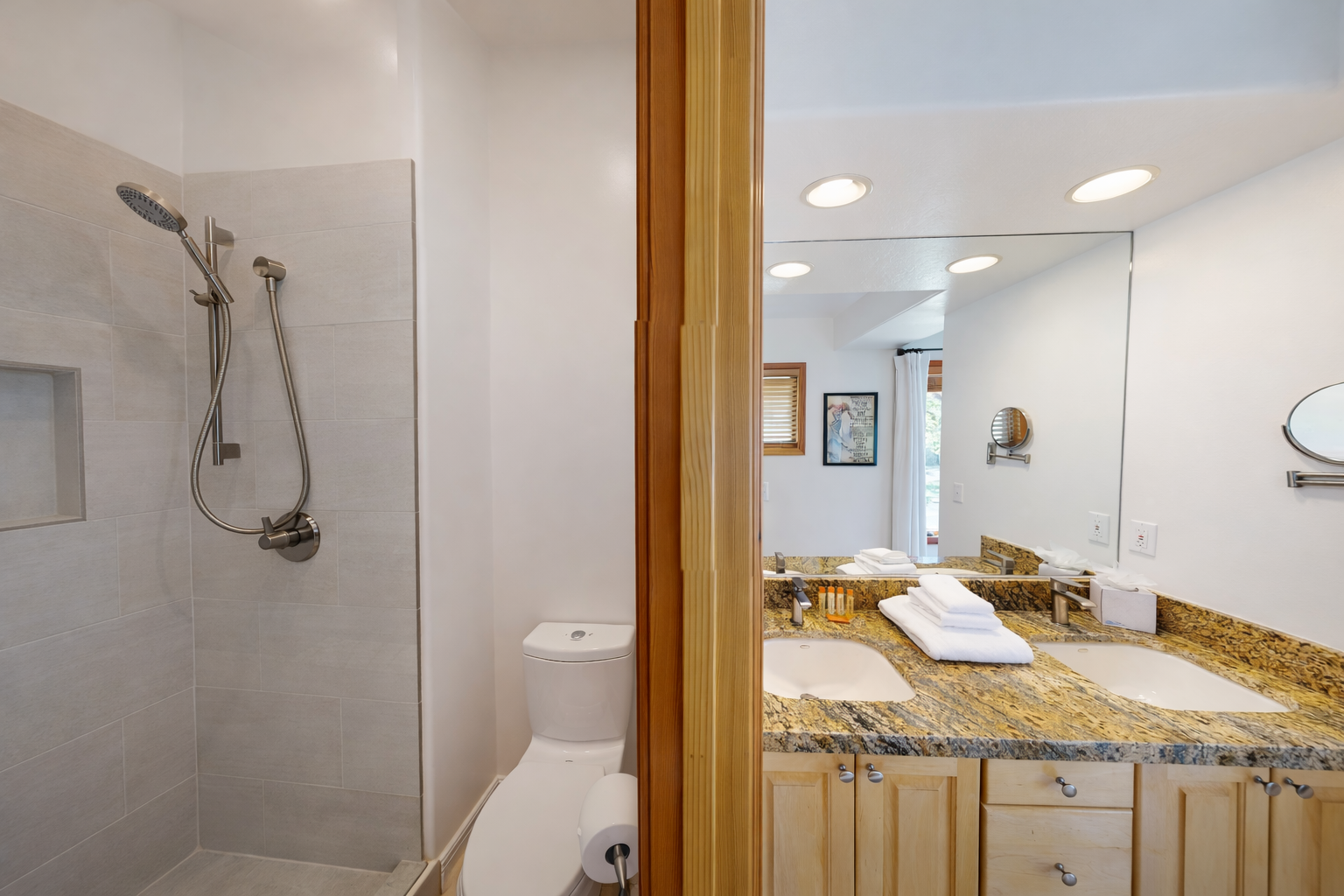 This modern bathroom features a spacious double vanity with elegant granite countertops, a large illuminated mirror, and a sleek, glass-enclosed shower for your convenience.