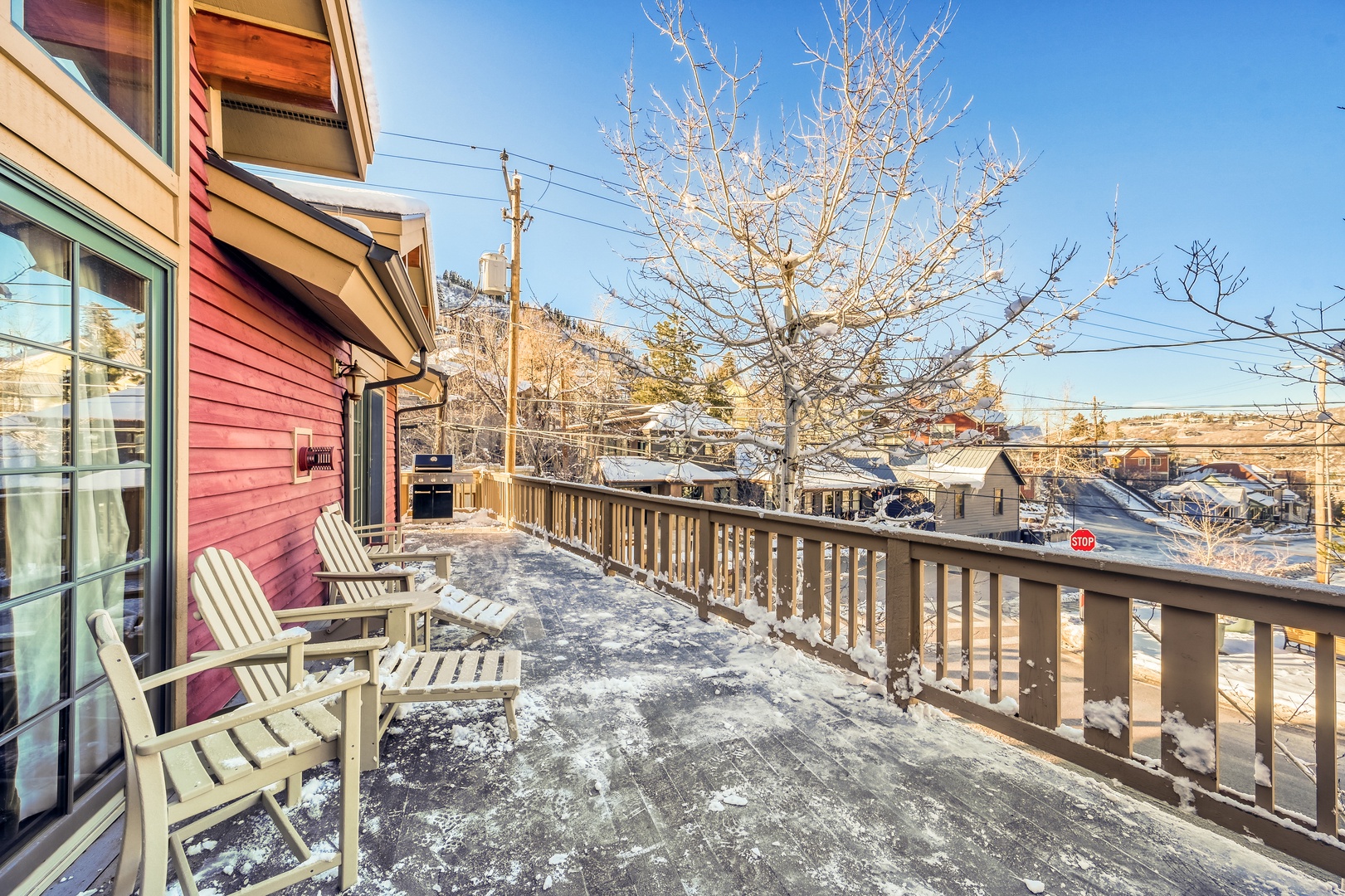 A spacious wooden deck features Adirondack chairs where you can enjoy crisp winter mornings with mountain views, warm sunlight, and peaceful neighborhood charm framed by snow-dusted trees.
