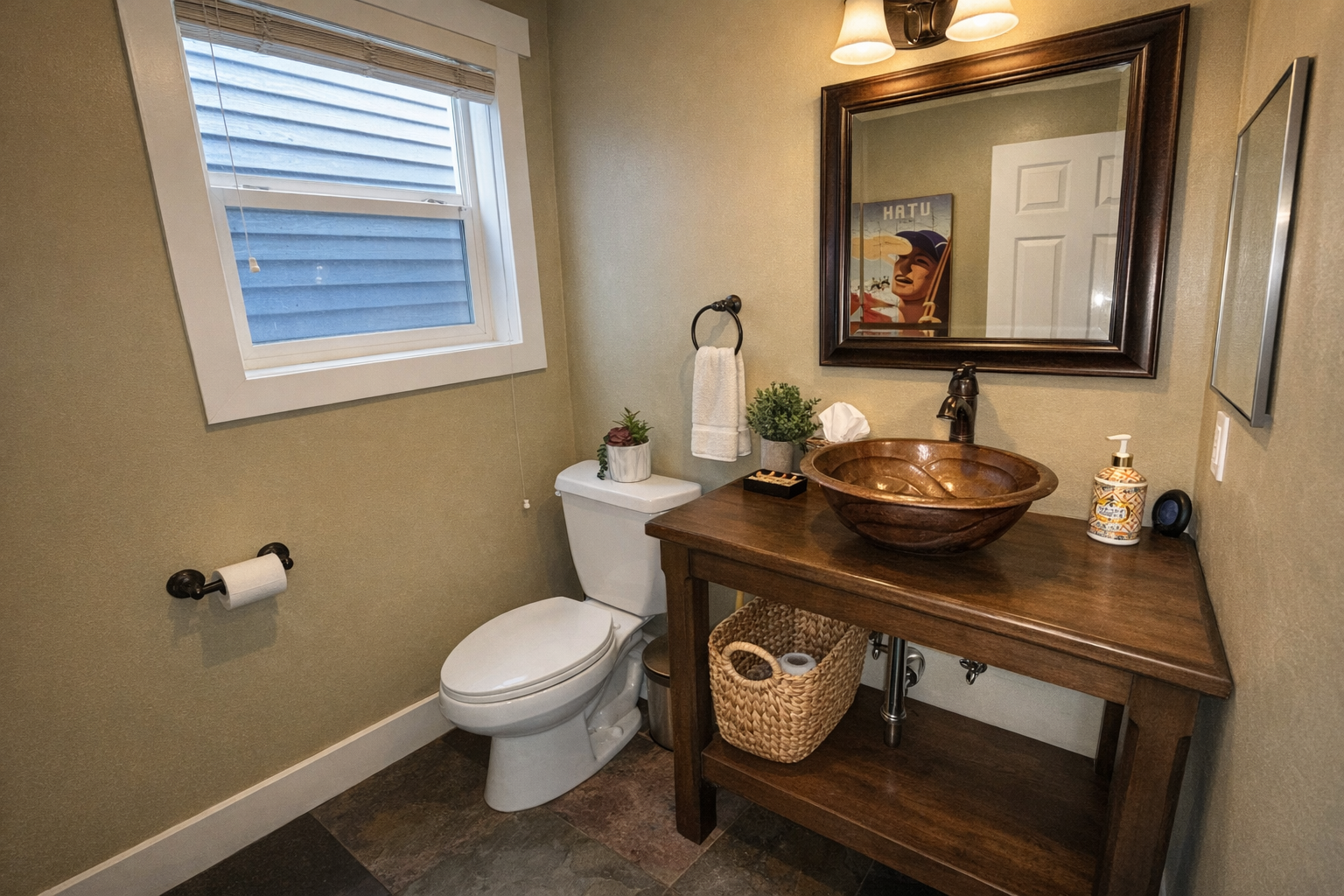 This charming powder room features a unique hammered copper vessel sink set on a rustic wooden vanity. Natural light from the window and warm overhead lighting create an inviting, stylish space.