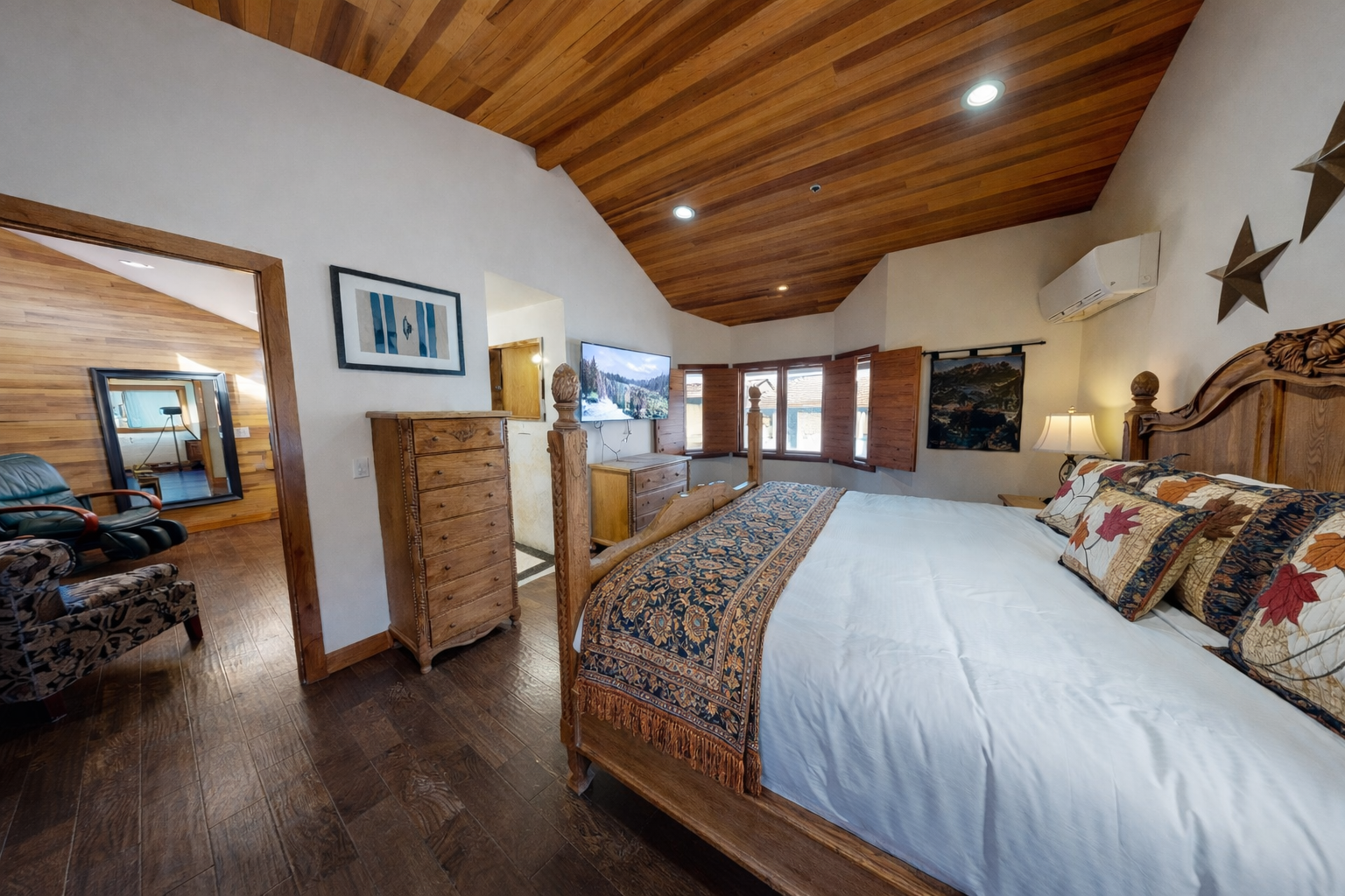 Relax in your spacious master bedroom featuring stunning wood beam ceilings, rustic furnishings, and modern amenities like AC and TV for the perfect mountain retreat.