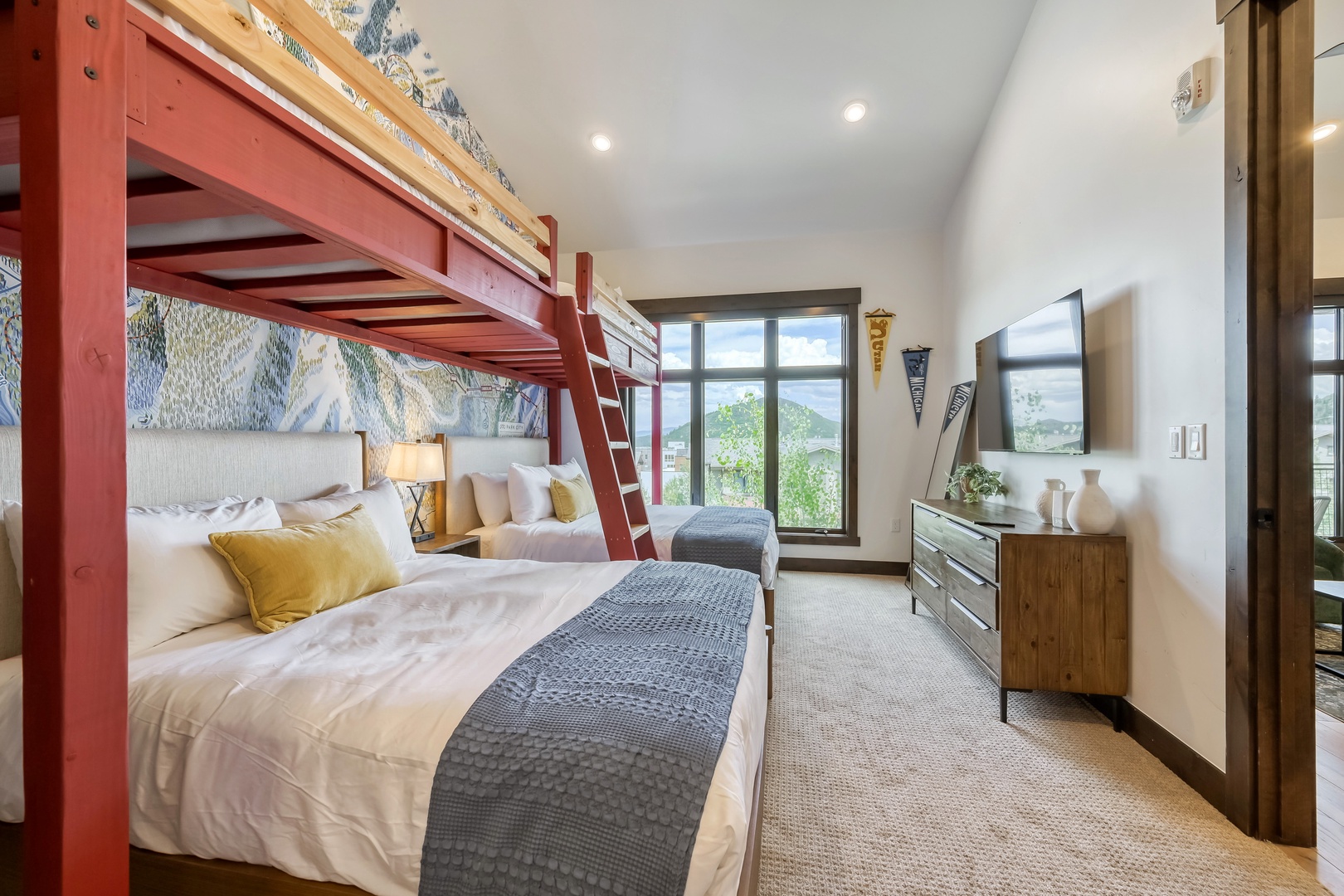 Relax in this thoughtfully designed room featuring cozy bunk beds, crisp linens, and stunning mountain views through expansive windows that frame the natural beauty beyond.