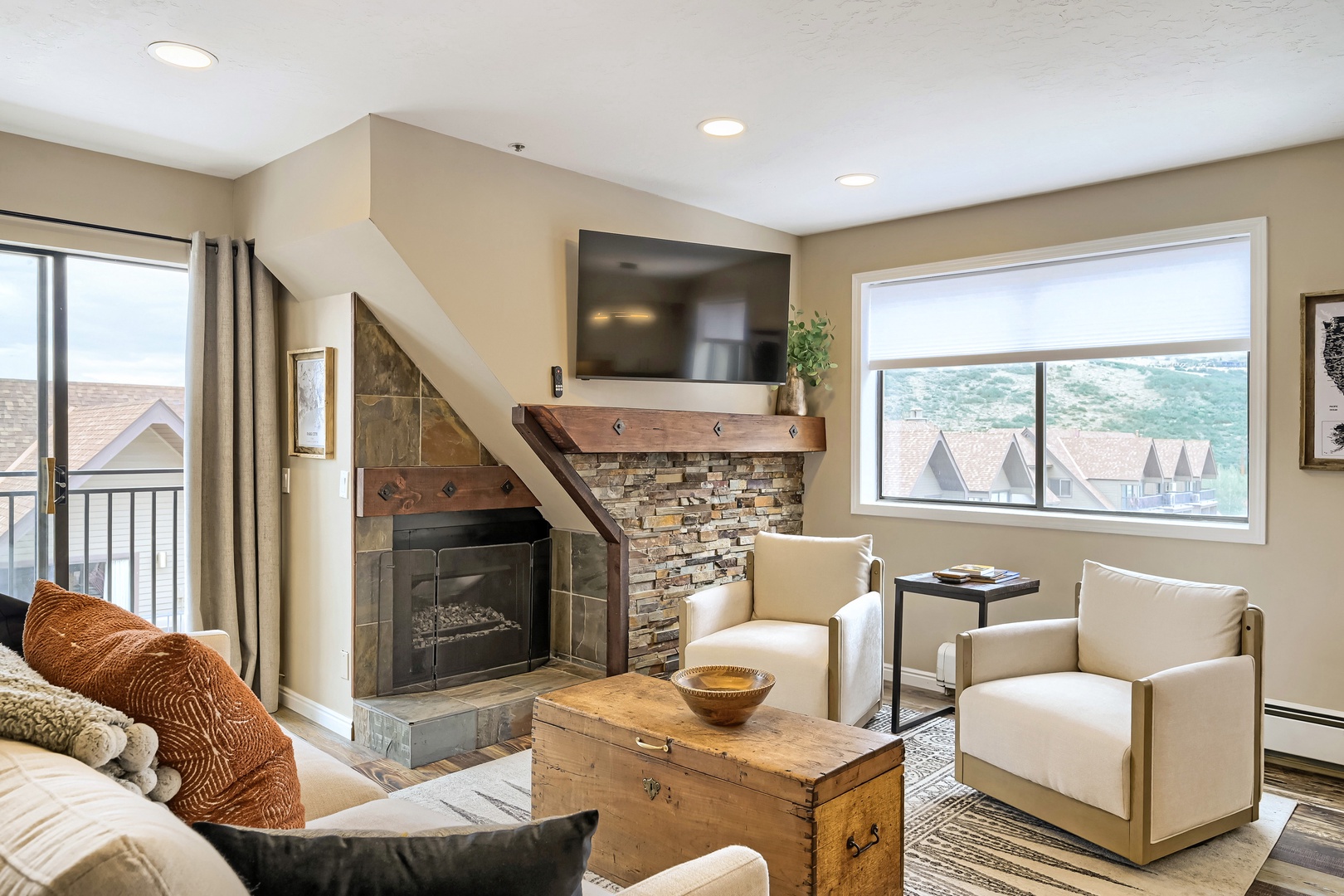 Settle into your cozy living room where a stone fireplace adds warmth and character. Natural light streams through large windows framing peaceful hillside views, inviting you to relax and unwind.