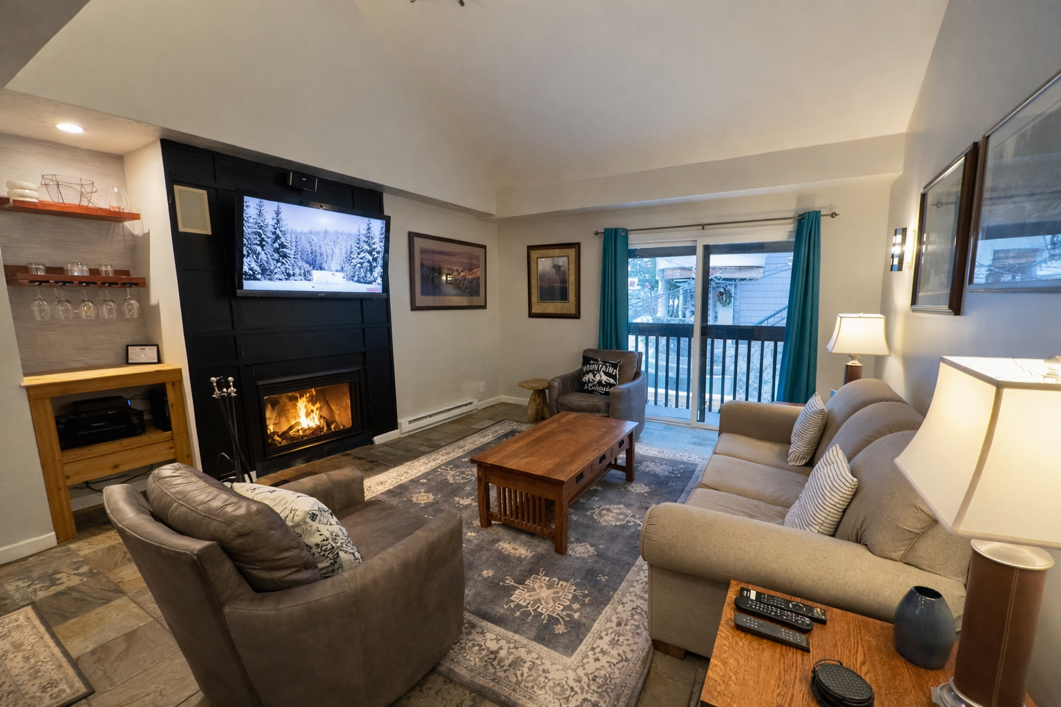 Cozy mountain living room with a stone fireplace, comfy sofa, and balcony access.