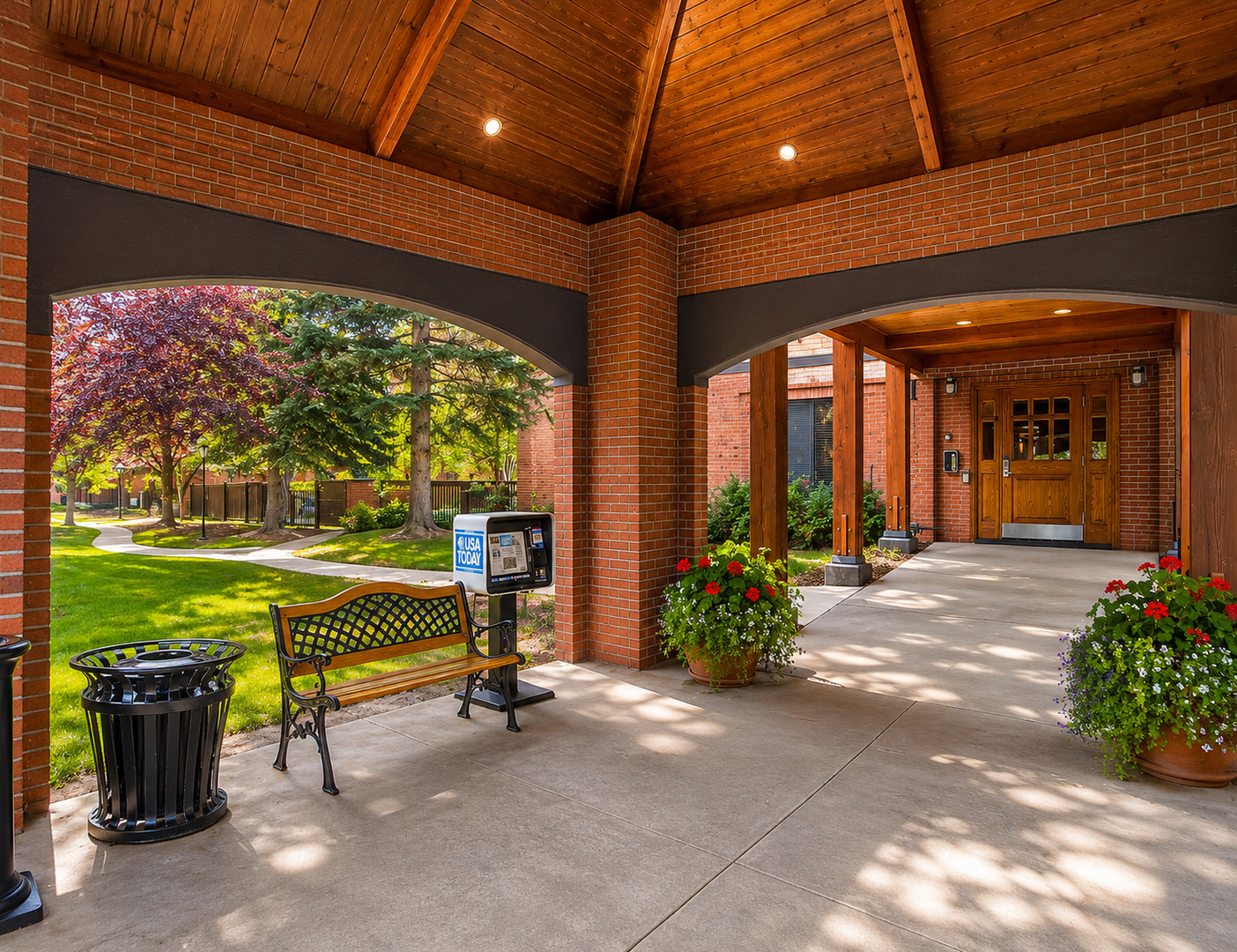 Park Station Entrance Courtyard. A welcoming covered entrance with brick arches and vaulted wood ceilings guides guests past vibrant potted flowers toward the property's main door, framed by lush landscaping and tree-lined grounds beyond.