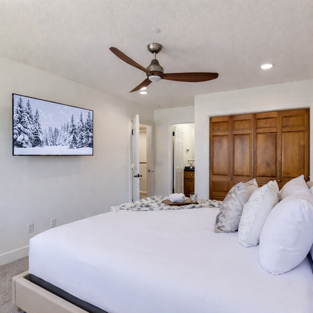 Retire to this quiet, modern bedroom featuring an upholstered king bed, large TV, soft lighting, and a ceiling fan, the perfect escape after a busy day.