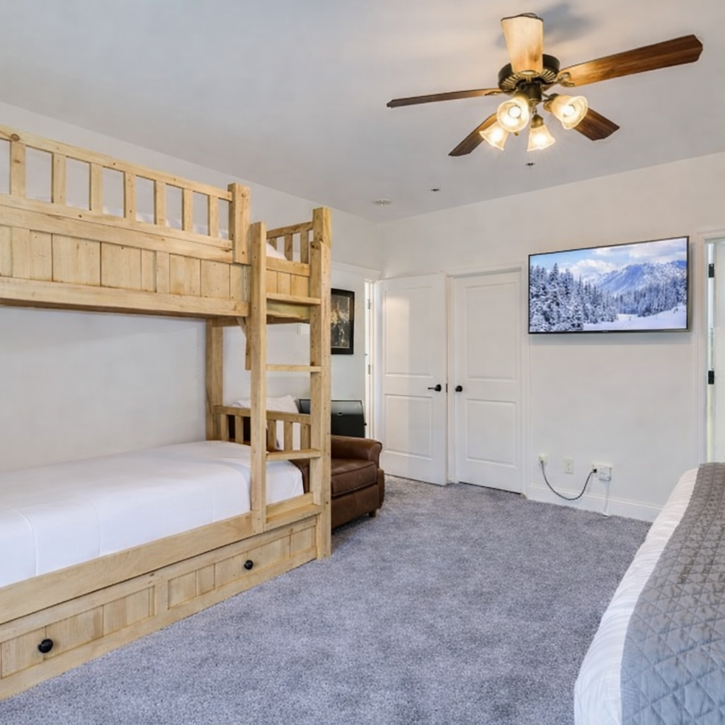 Spacious bunk room with custom wood bunks, plush carpeting, and wall-mounted TV. Perfect for families or groups, offering cozy comfort.