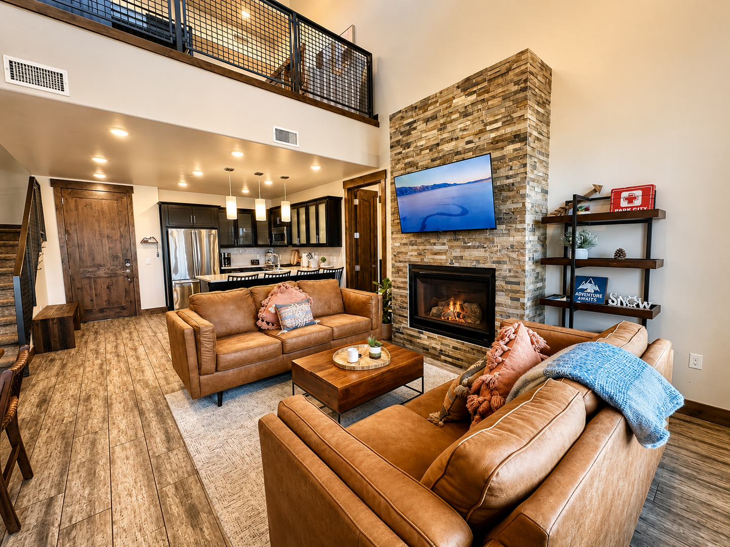 Relax in this luxurious open-concept living area. It features a stunning floor-to-ceiling stone fireplace, plush leather seating, and a modern kitchen with high-end finishes, perfect for mountain getaways.