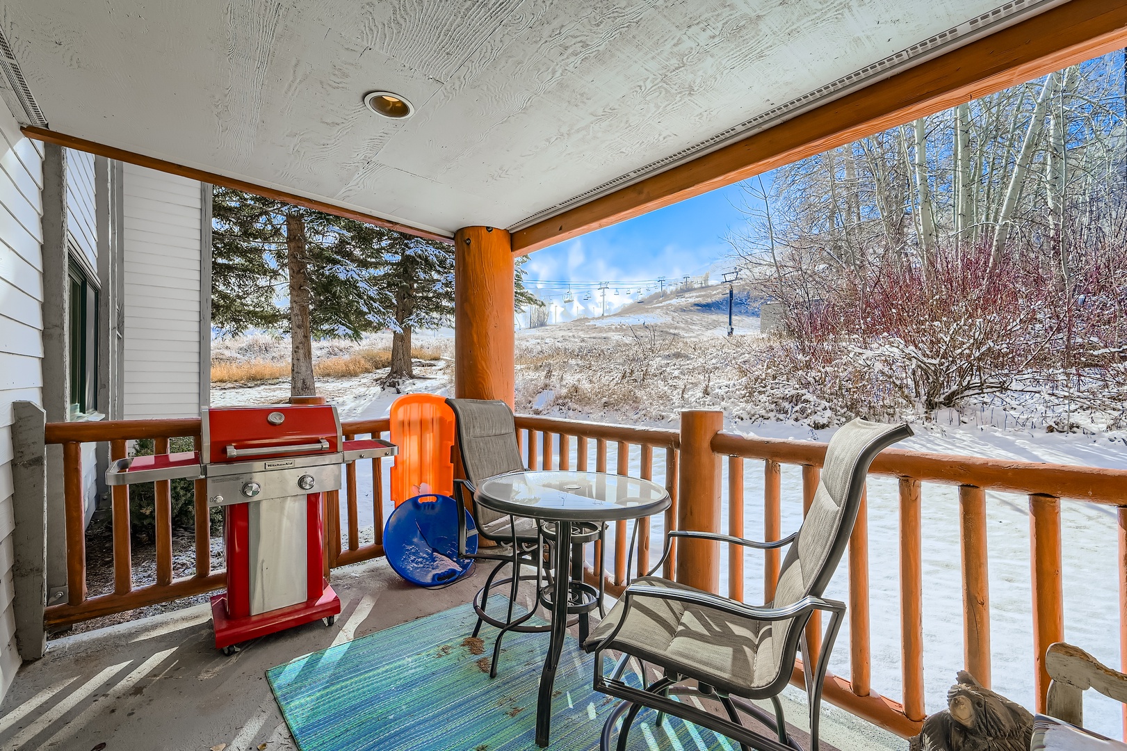 Covered patio with gas grill, ski slope views, and cozy seating—your perfect spot for morning coffee or après-ski relaxation in the snowy mountain air.